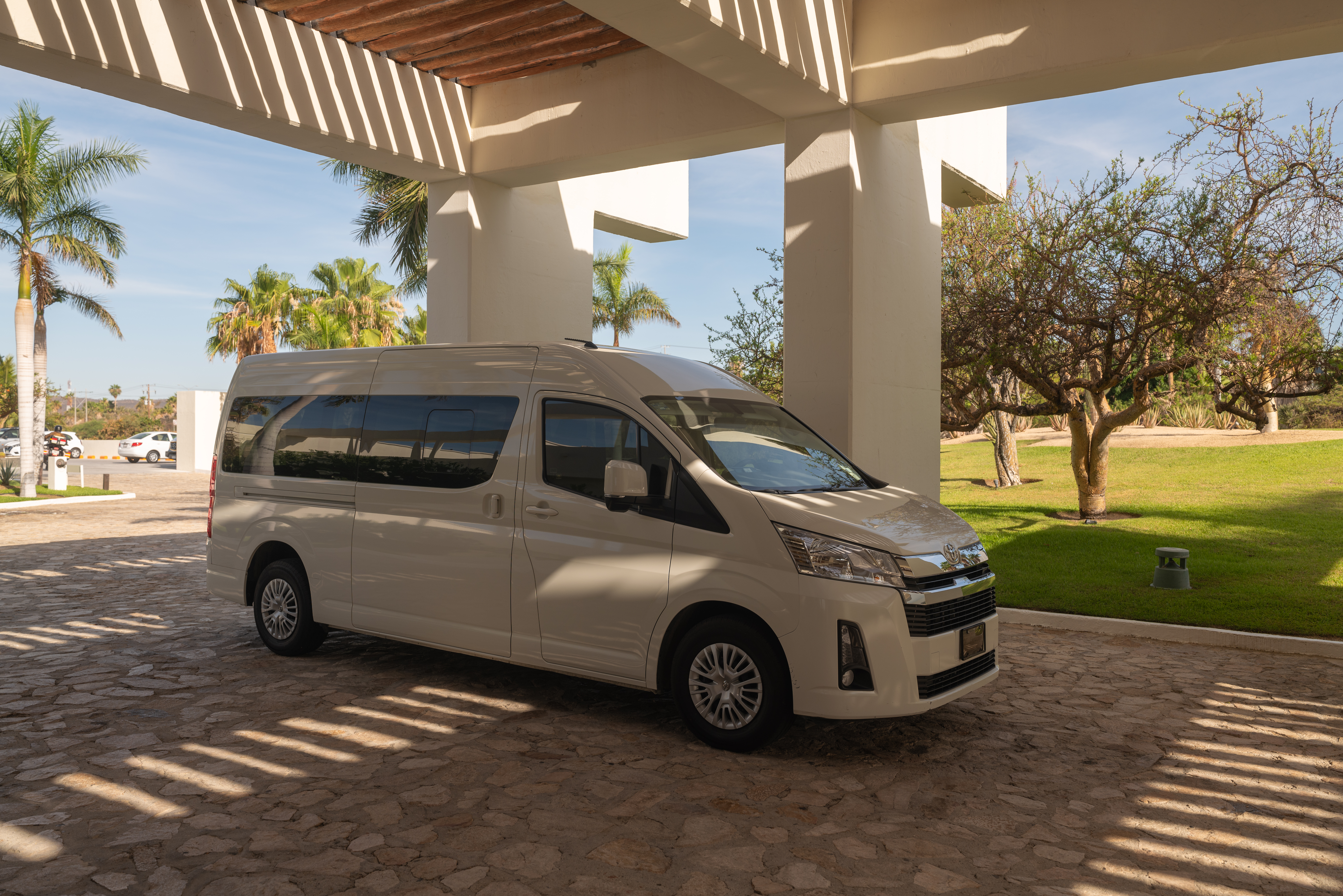 White passenger shuttle van at a sunny resort entrance with palm trees.