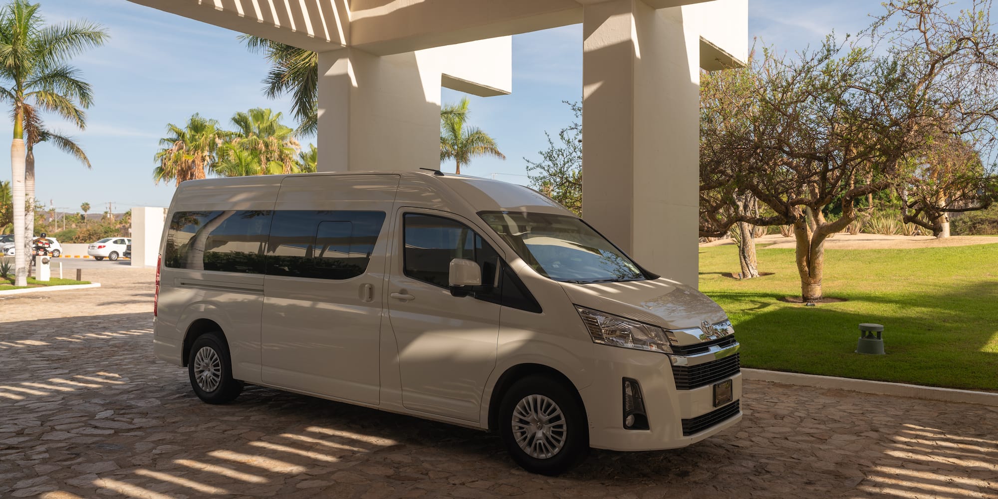 White passenger shuttle van at a sunny resort entrance with palm trees.