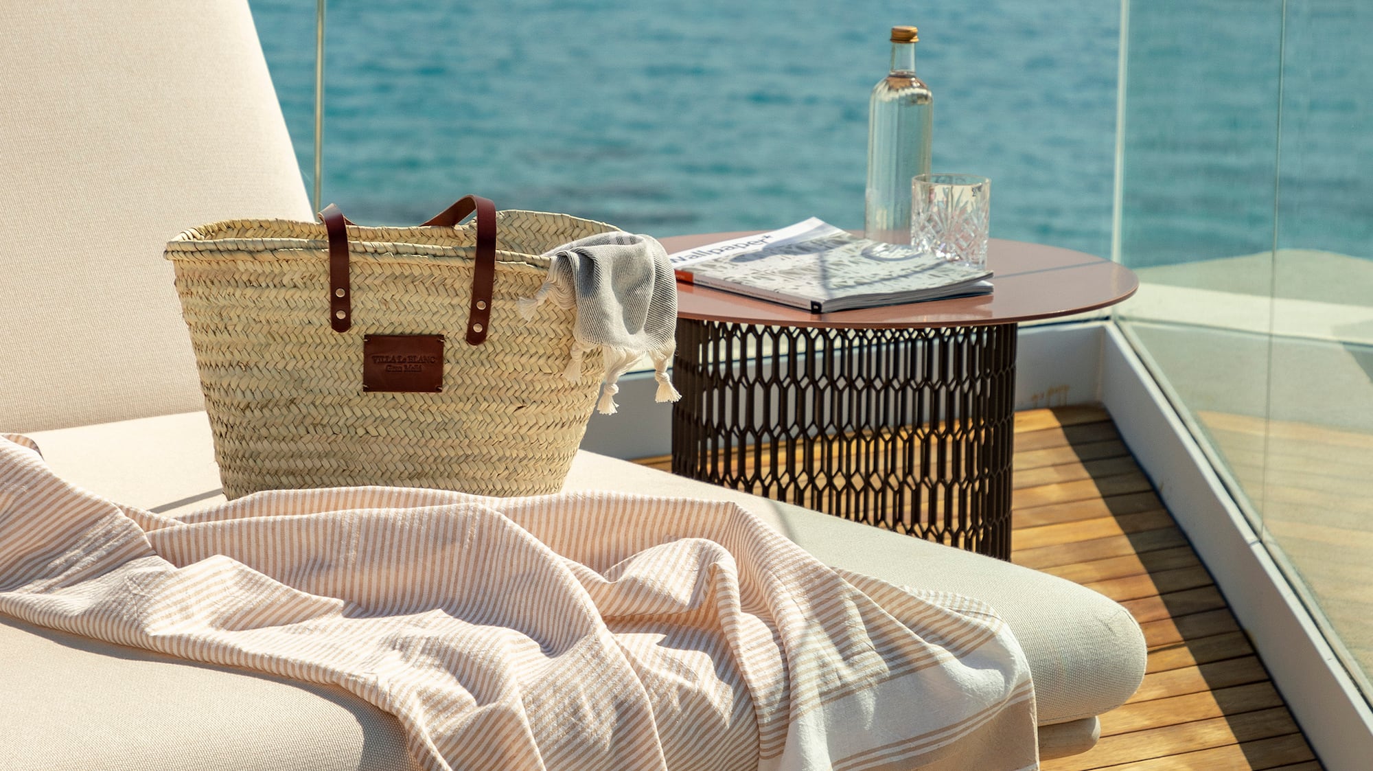 a beach chair with a towel and a bag on a deck overlooking the water