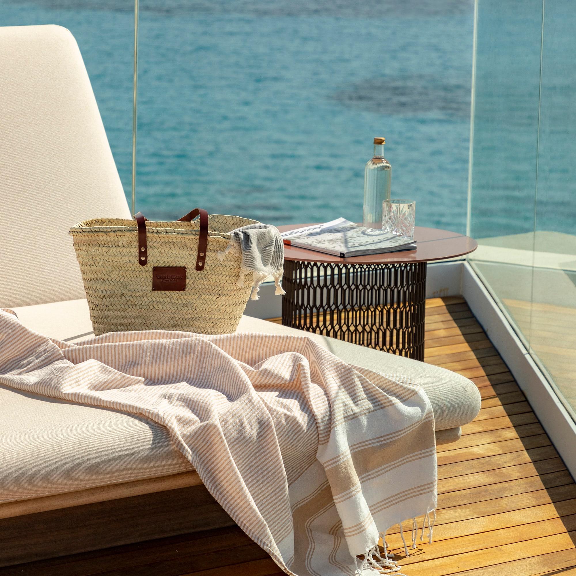 a beach chair with a towel and a bag on a deck overlooking the water