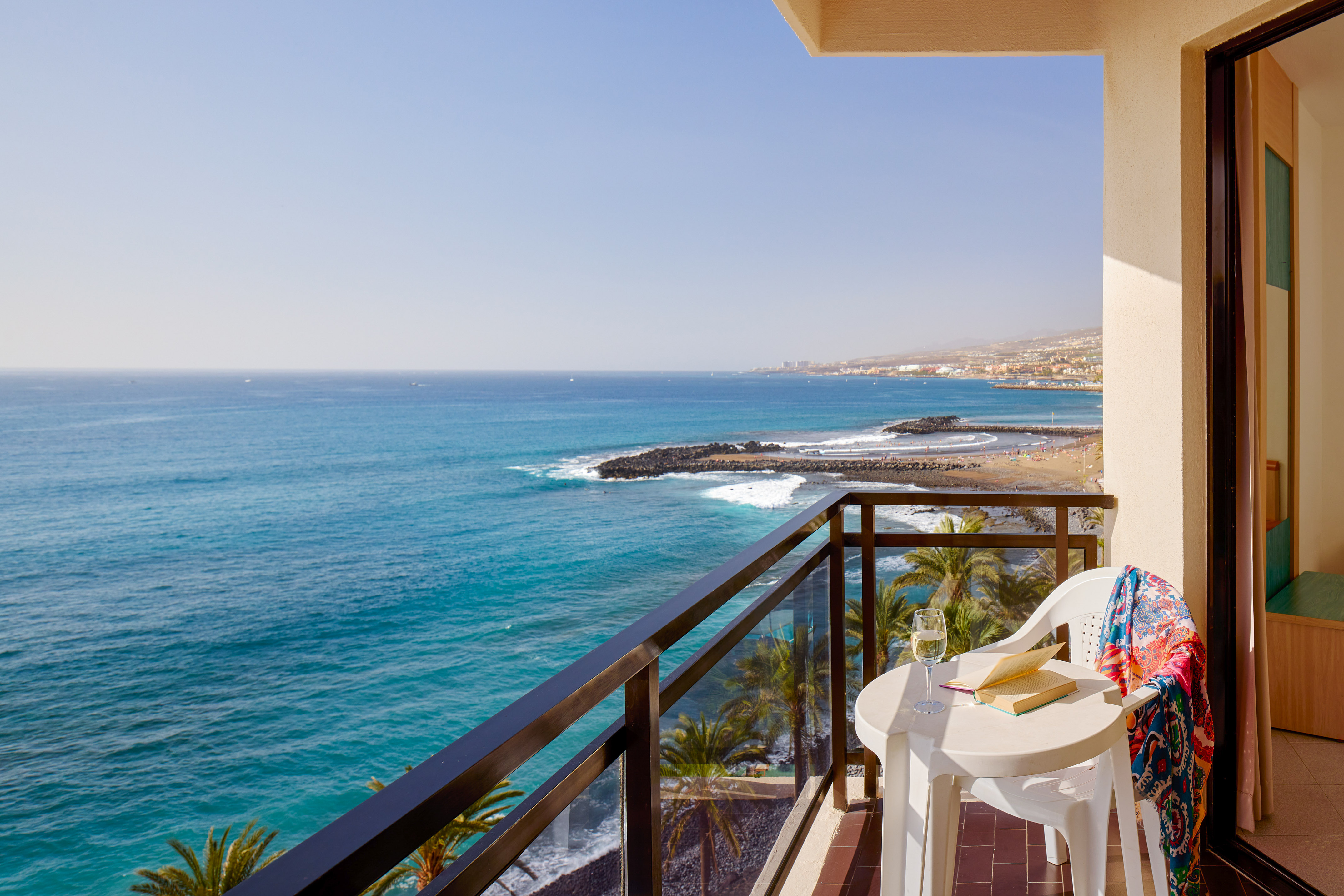 Ocean view balcony with book, wine, beach, and coastal resort.