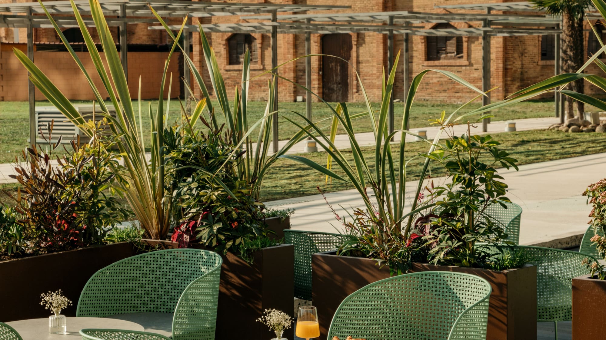 Desayuno en terraza moderna con sillas verdes y edificio de ladrillo.