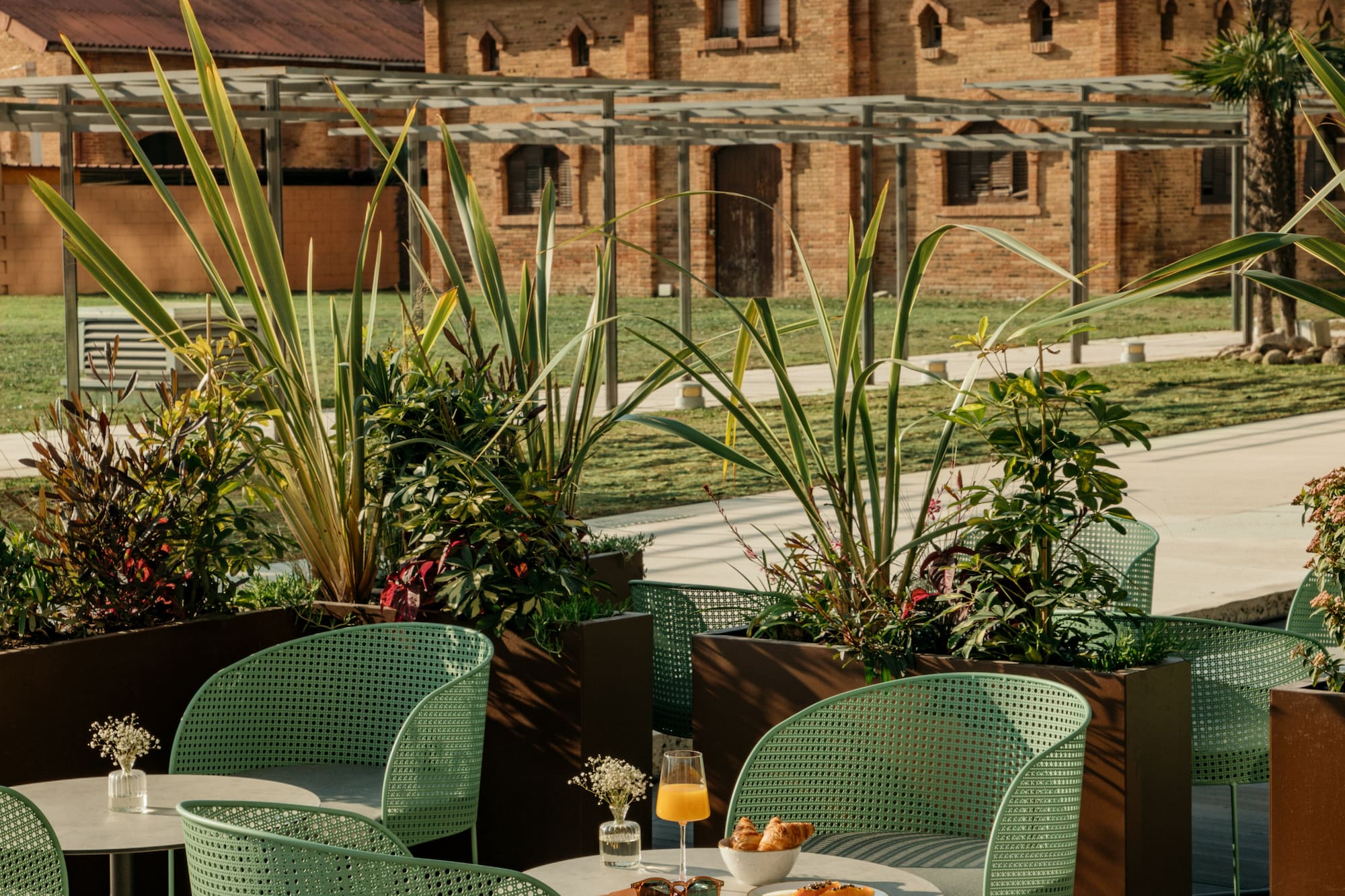 Desayuno en terraza moderna con sillas verdes y edificio de ladrillo.