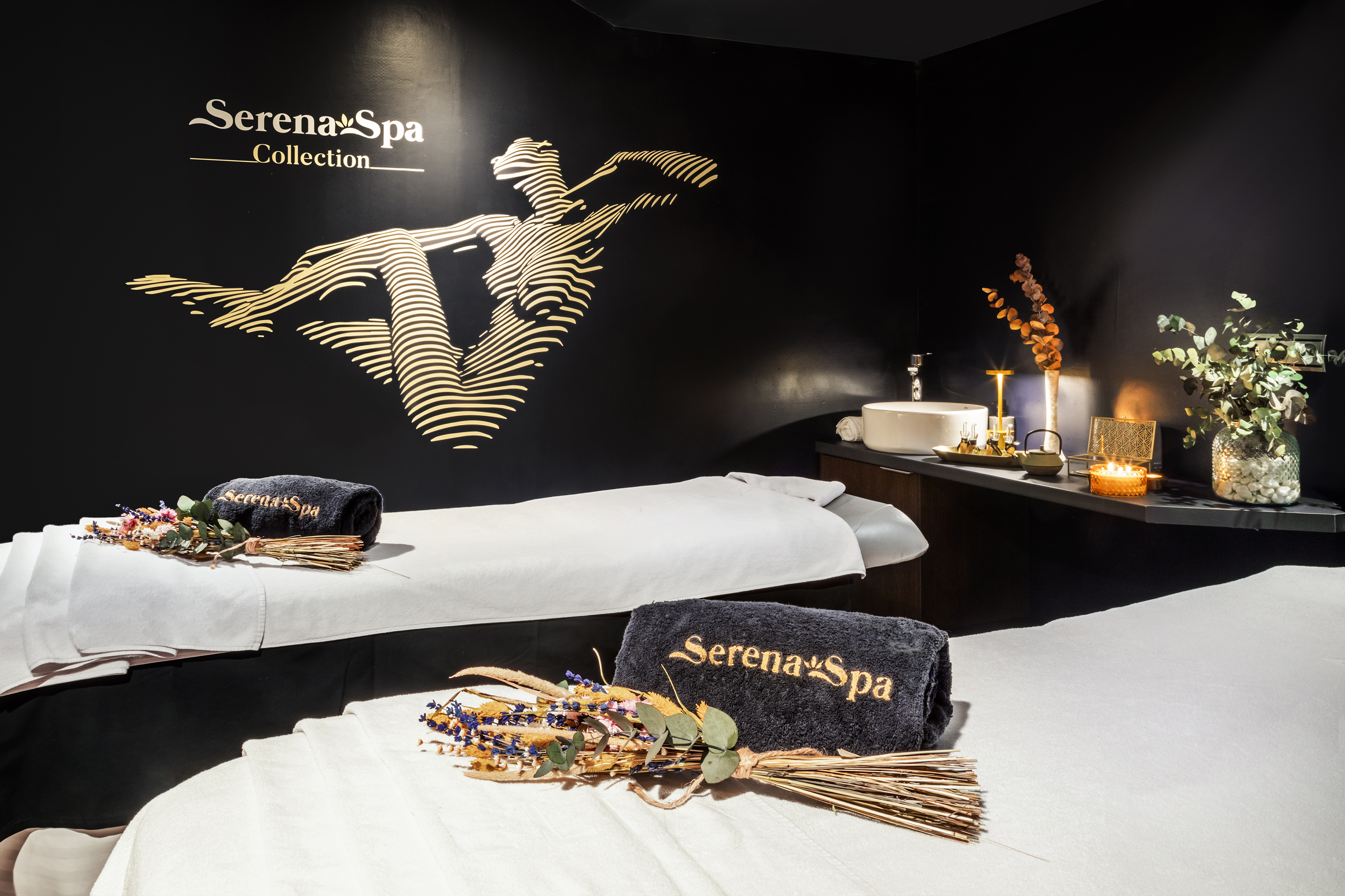Serena Spa treatment room with two massage beds, branded towels, and gold wall art.