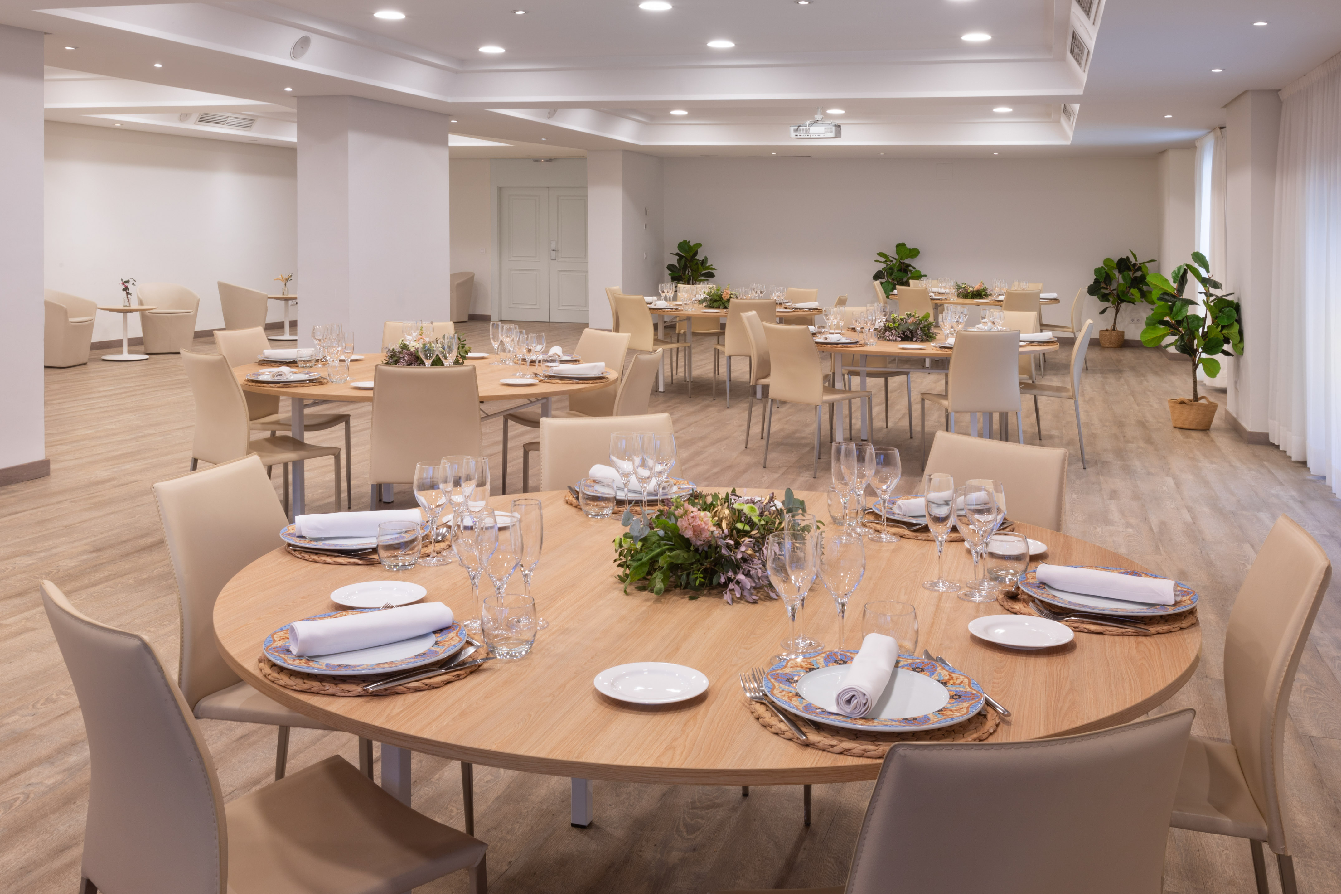 Hotel event space with round dining tables, place settings, and beige chairs.