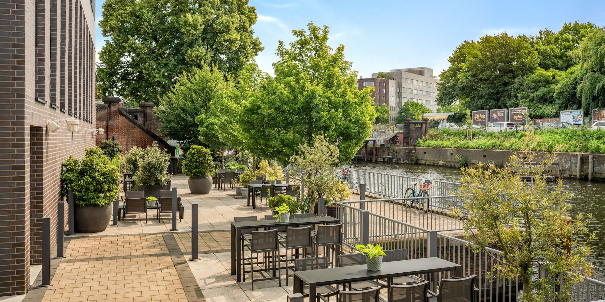 a patio with tables and chairs and trees by a river