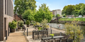 a patio with tables and chairs and trees by a river