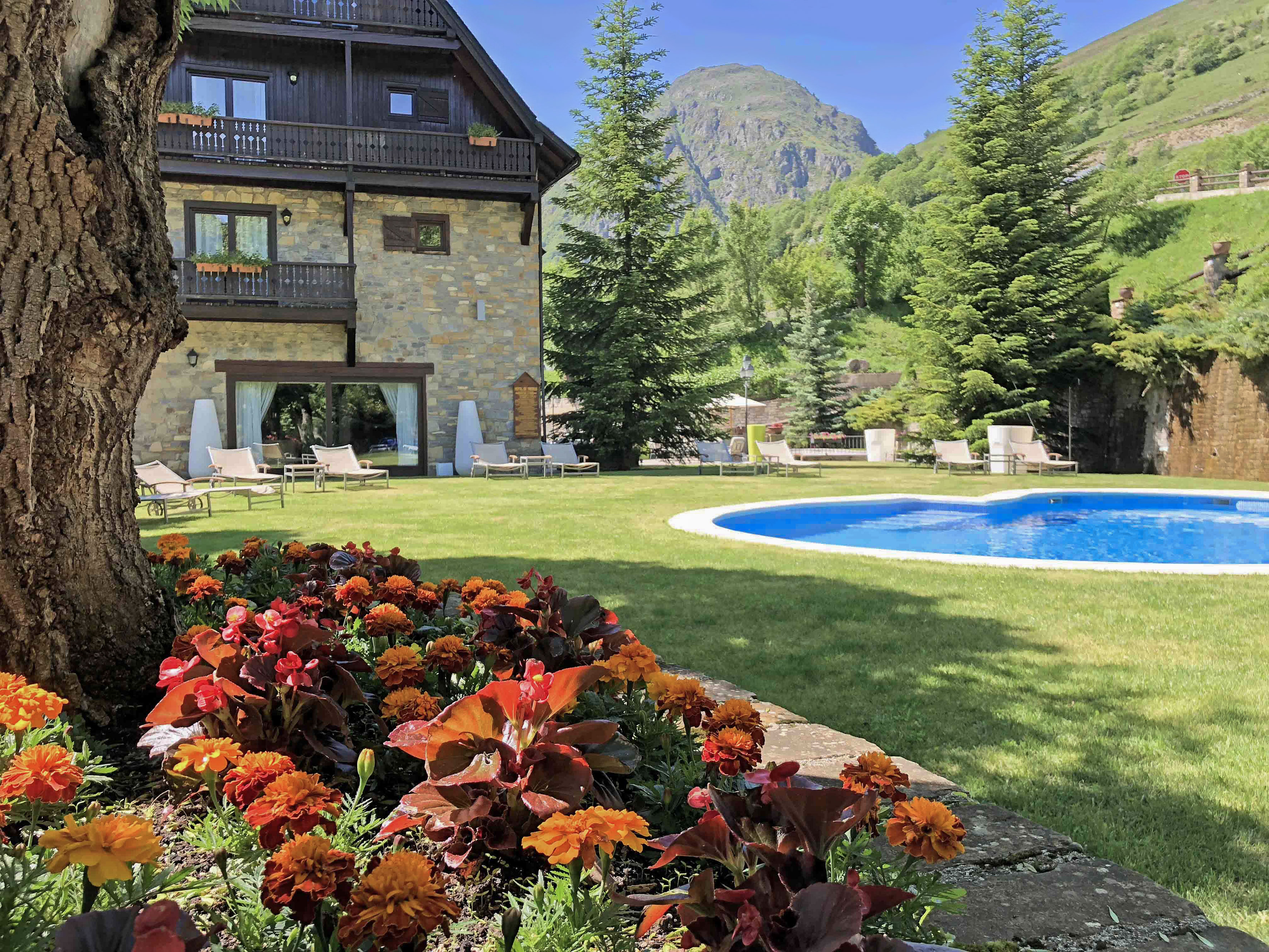 Hotel de montaña con piscina, jardín y montañas verdes.