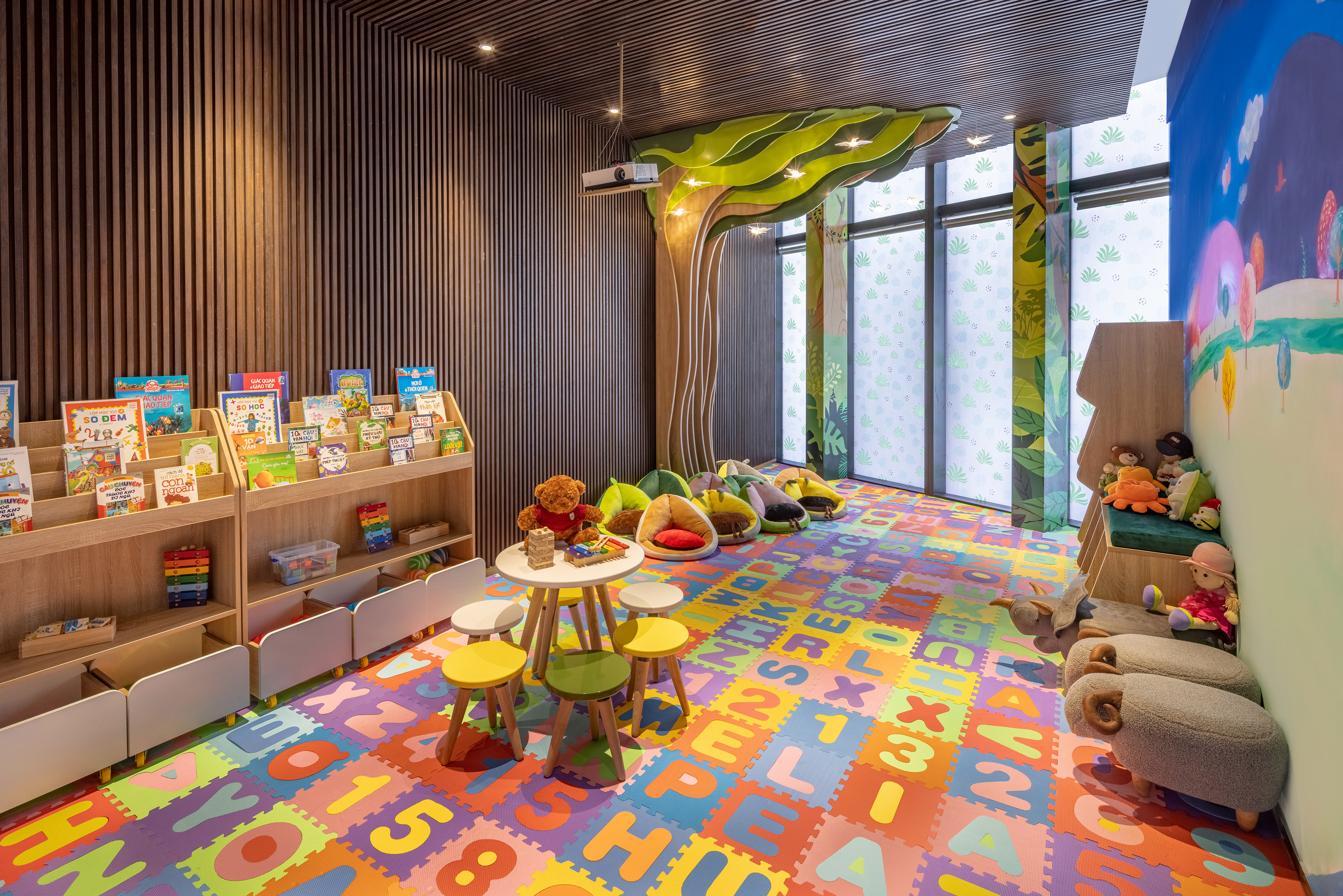 Vibrant kids' library with alphabet floor, books, tree mural, and soft seating.