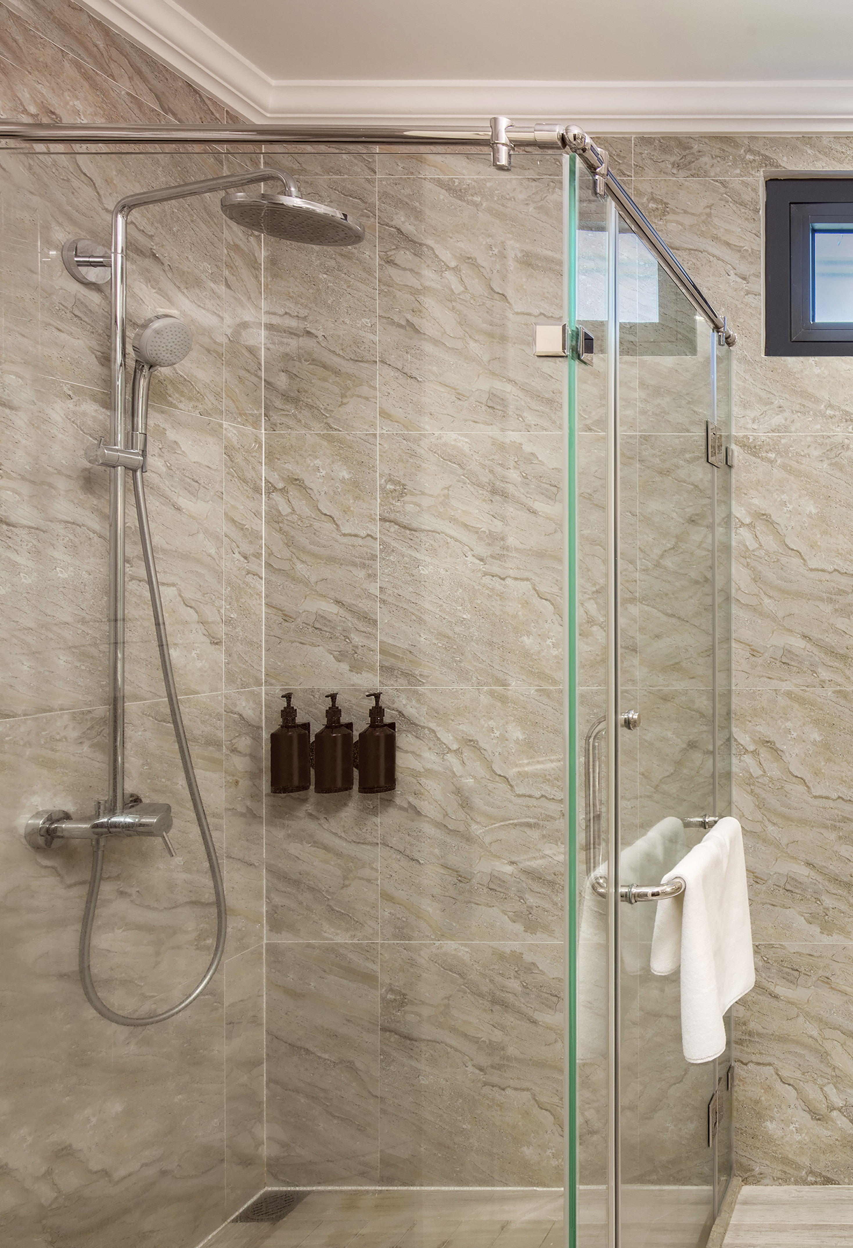 Glass shower enclosure with rain showerhead, handheld, and tan tiled walls.