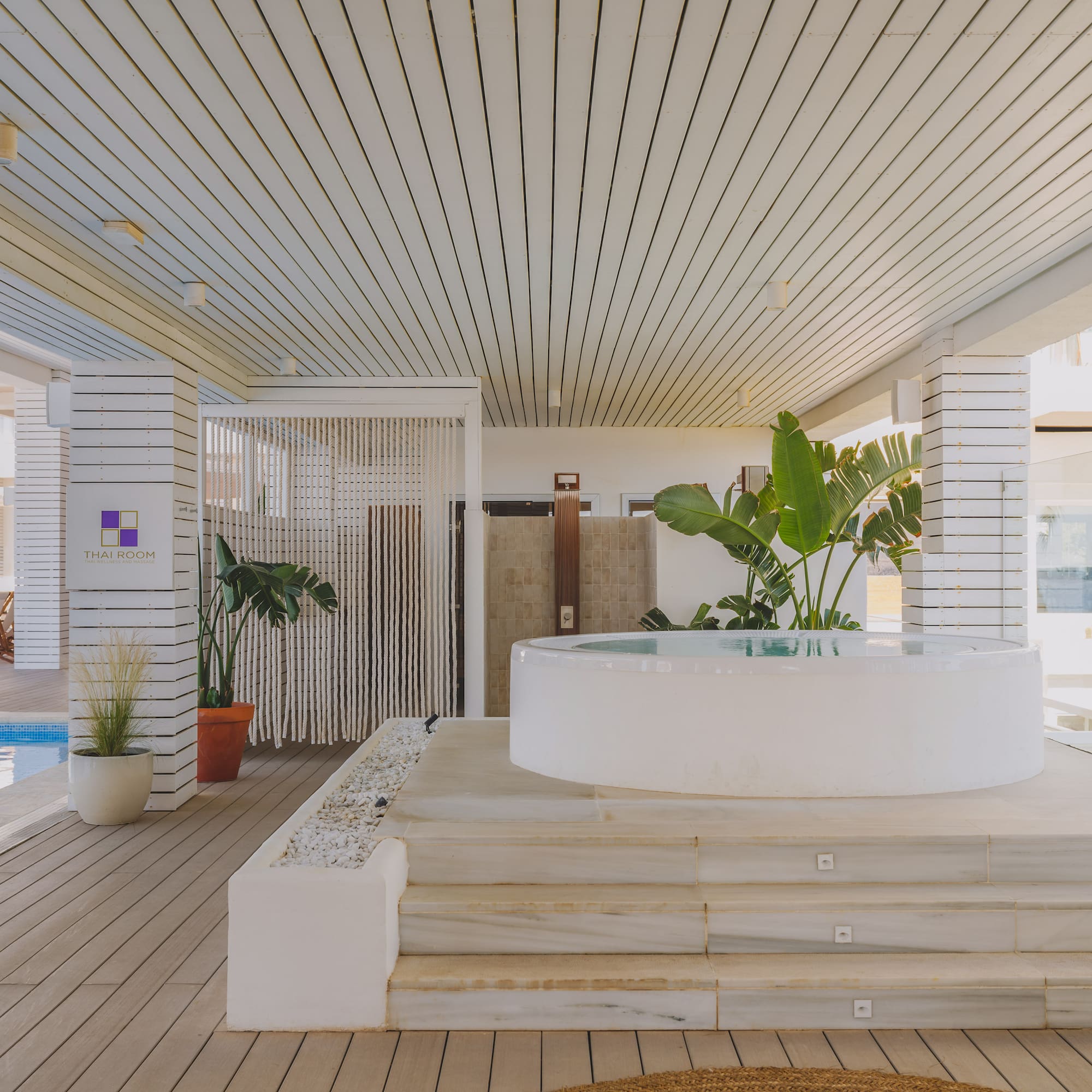 Resort spa with white round hot tub, pool, wooden deck, and Thai Room sign.