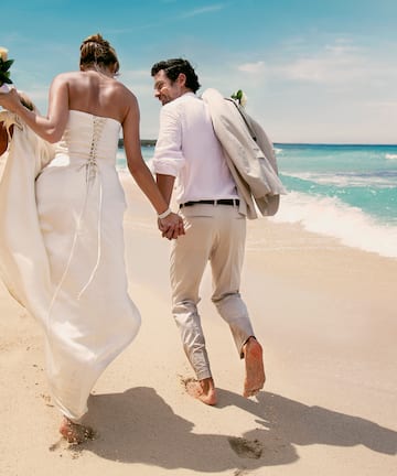 a man and woman holding hands and walking on a beach