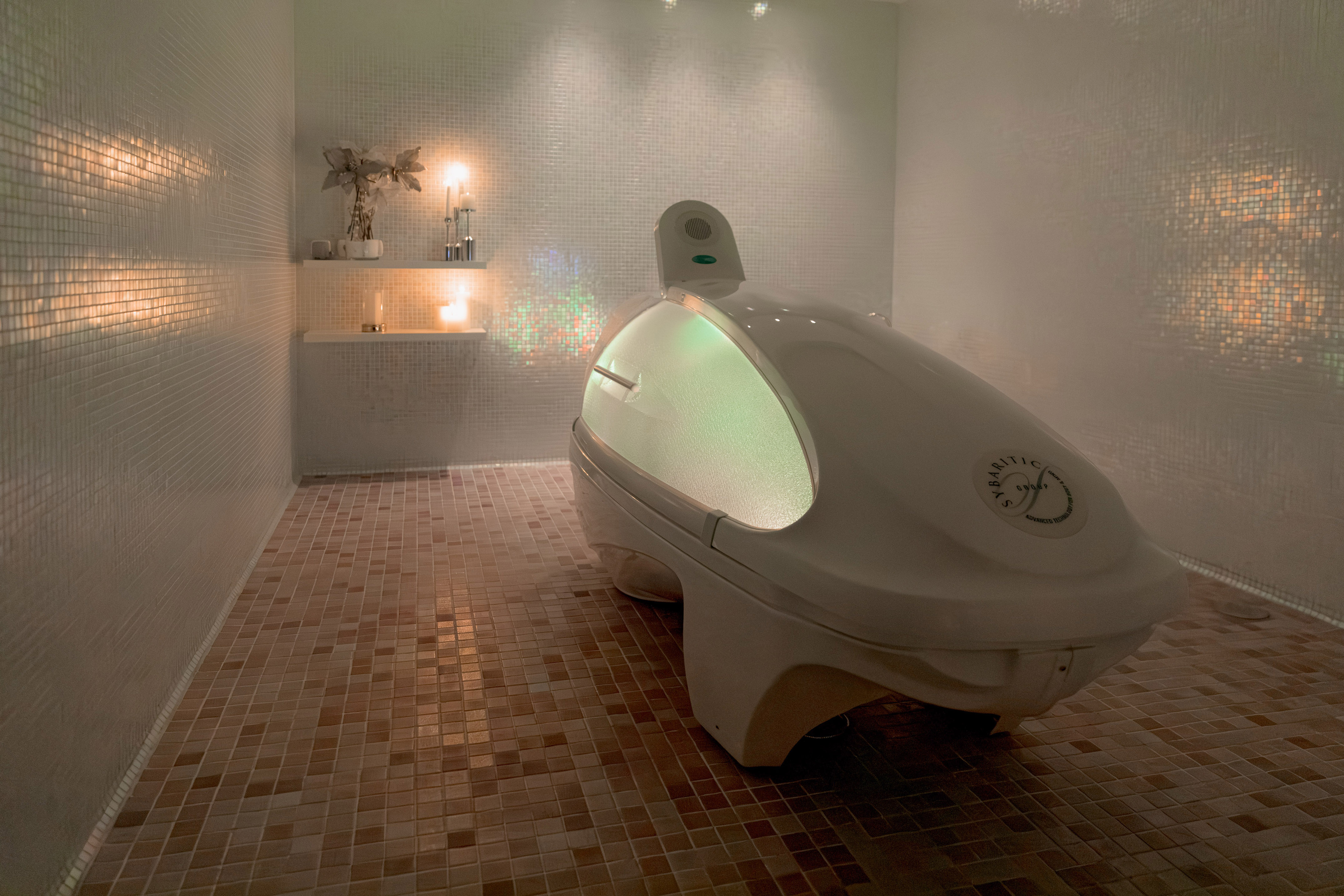 Sybaritic spa pod with green light in a mosaic-tiled hydrotherapy room.