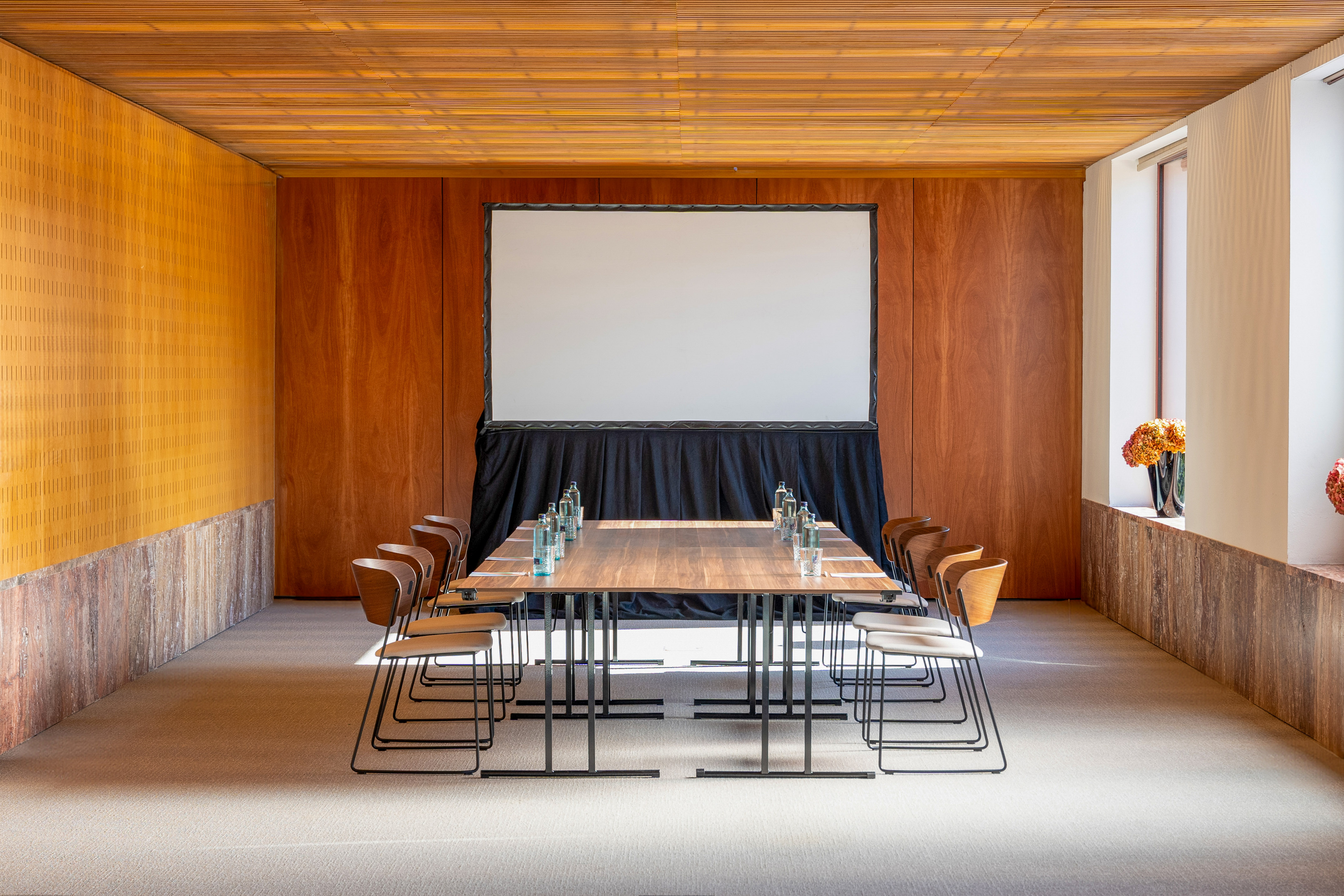 Modern meeting room with wood walls, long table, chairs, and projector screen.