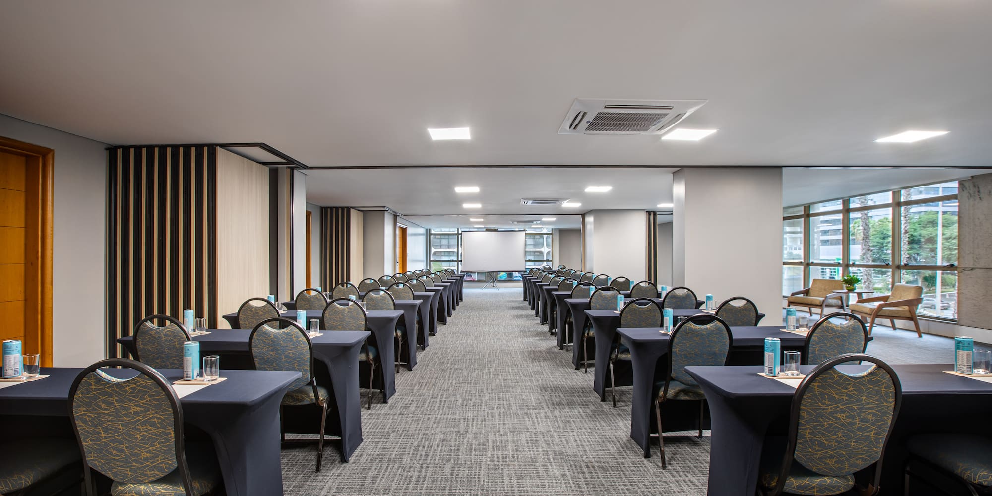 Modern conference room setup with tables, chairs, projector screen, windows.