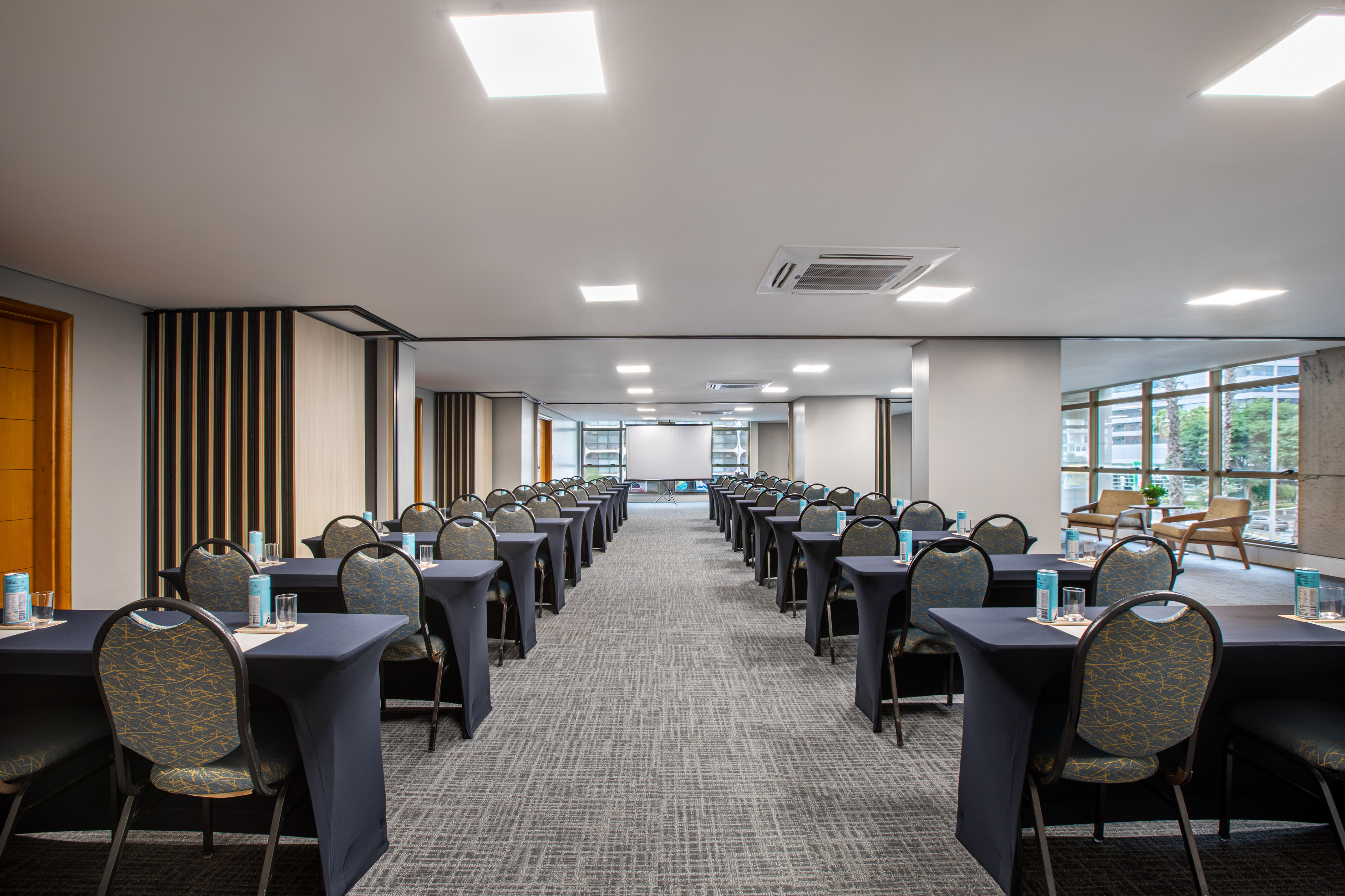 Modern conference room setup with tables, chairs, projector screen, windows.