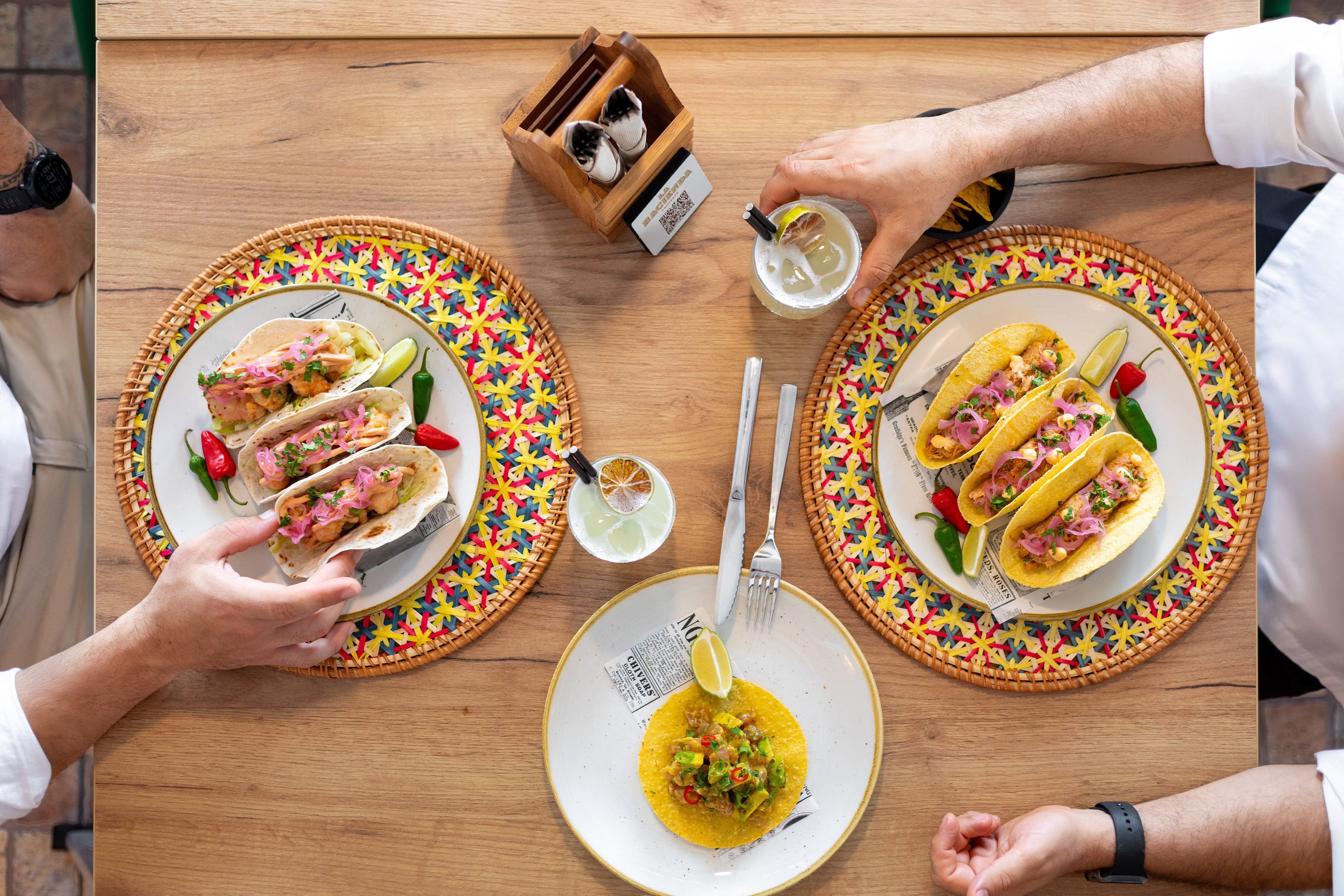 Shrimp and hard shell tacos, guacamole, and cocktails on a wooden table.