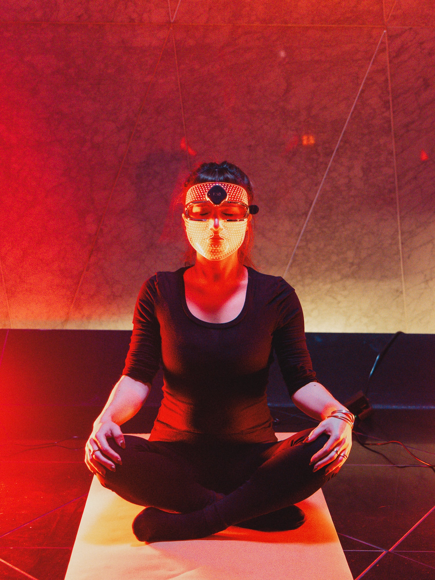 Woman meditating with futuristic LED light therapy mask in red light.