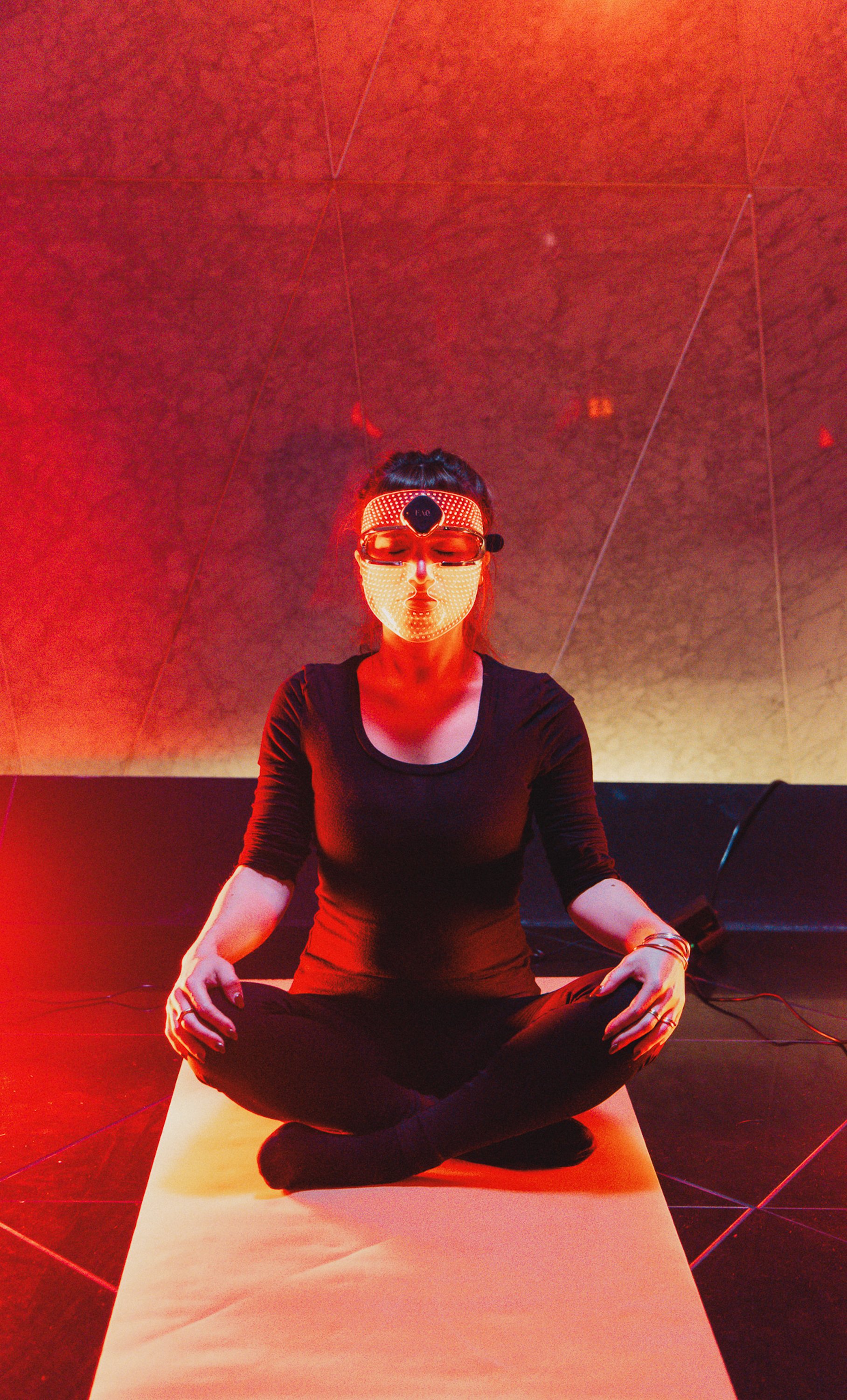 Woman meditating with futuristic LED light therapy mask in red light.