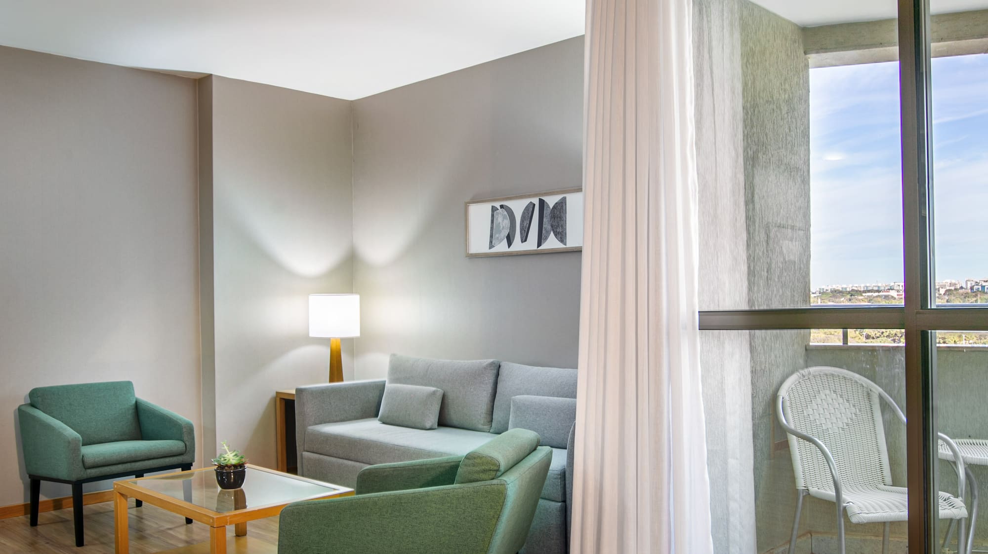 Modern living room with gray sofa, green armchairs, wood floor, and balcony.