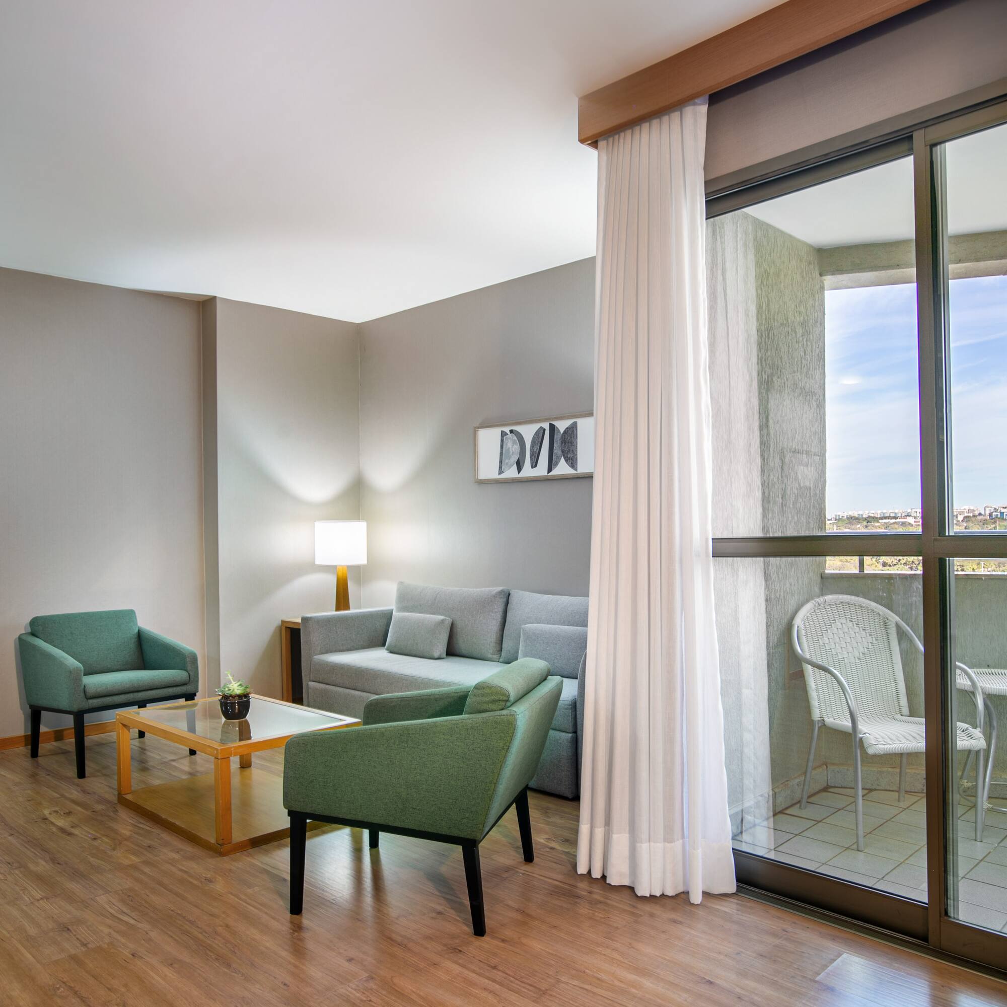 Modern living room with gray sofa, green armchairs, wood floor, and balcony.