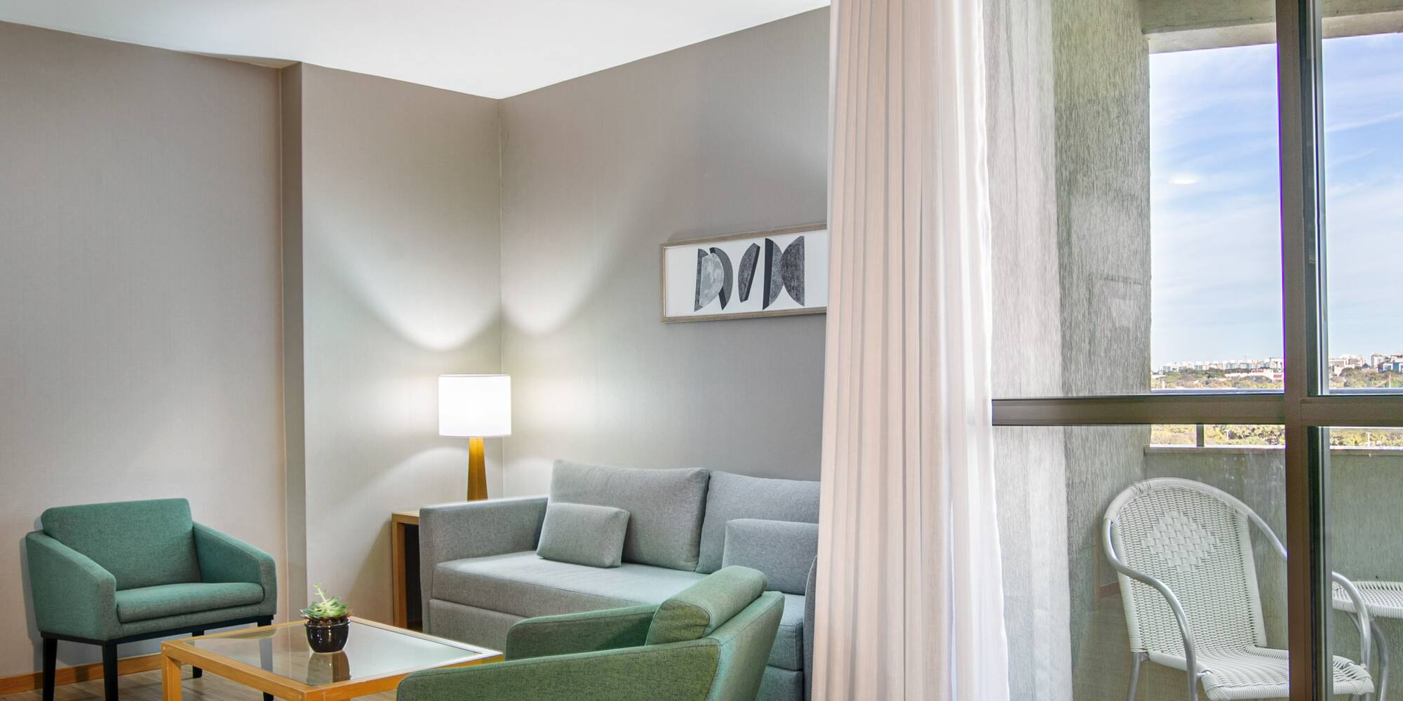Modern living room with gray sofa, green armchairs, wood floor, and balcony.