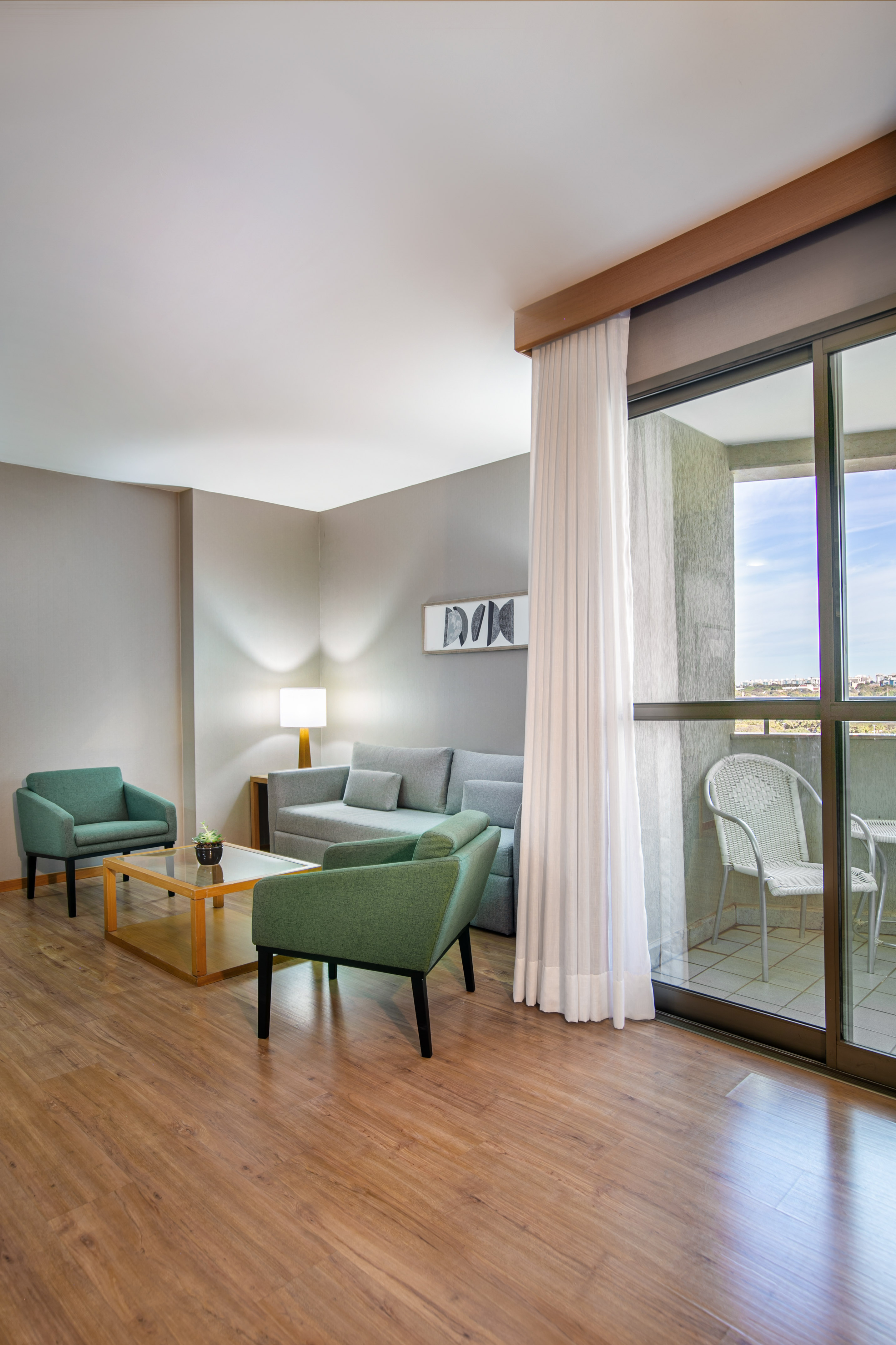 Modern living room with gray sofa, green armchairs, wood floor, and balcony.
