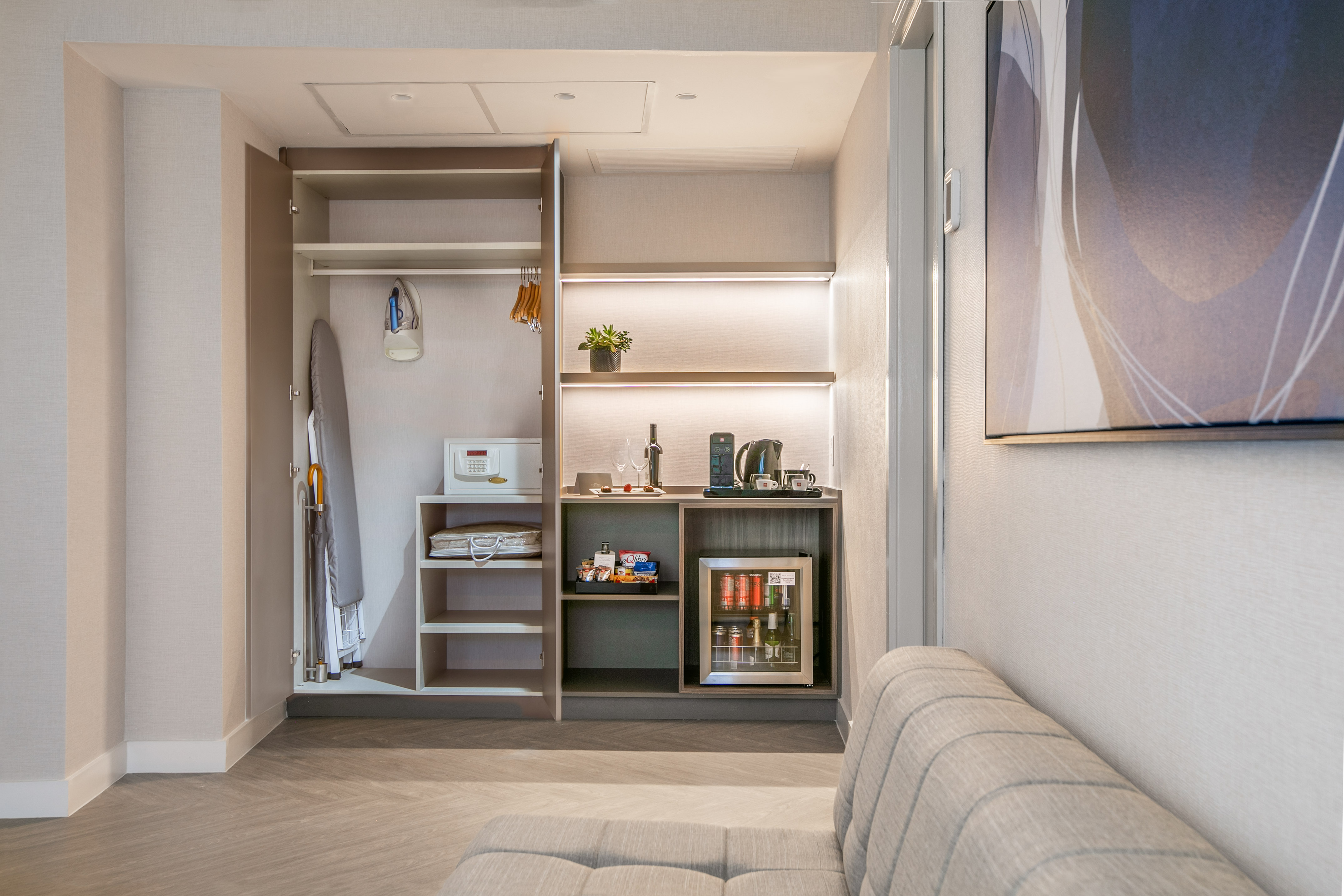 Hotel room wardrobe with minibar, coffee station, safe, and ironing amenities.