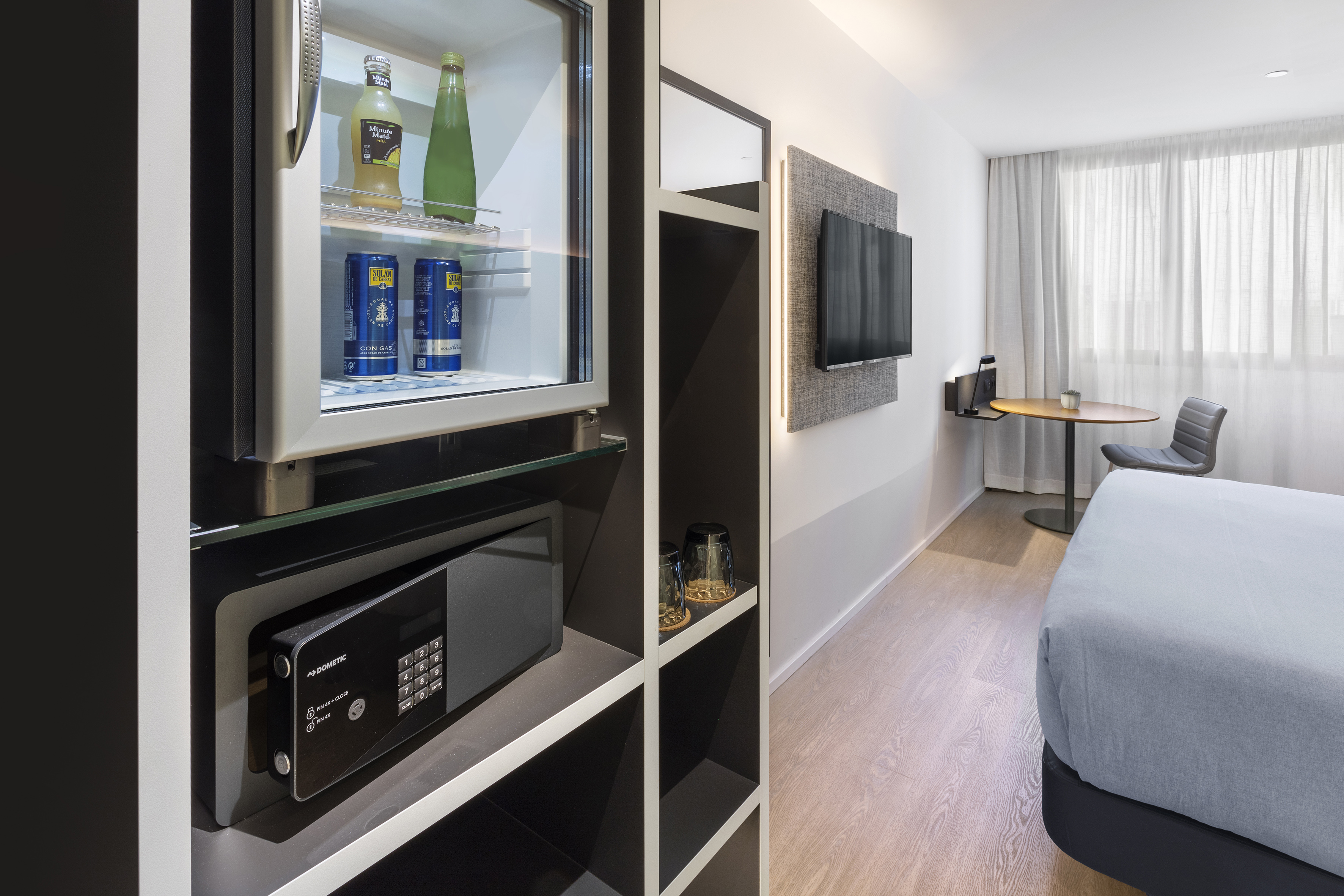 Modern hotel room with minibar, safe, wall-mounted TV, and bed.