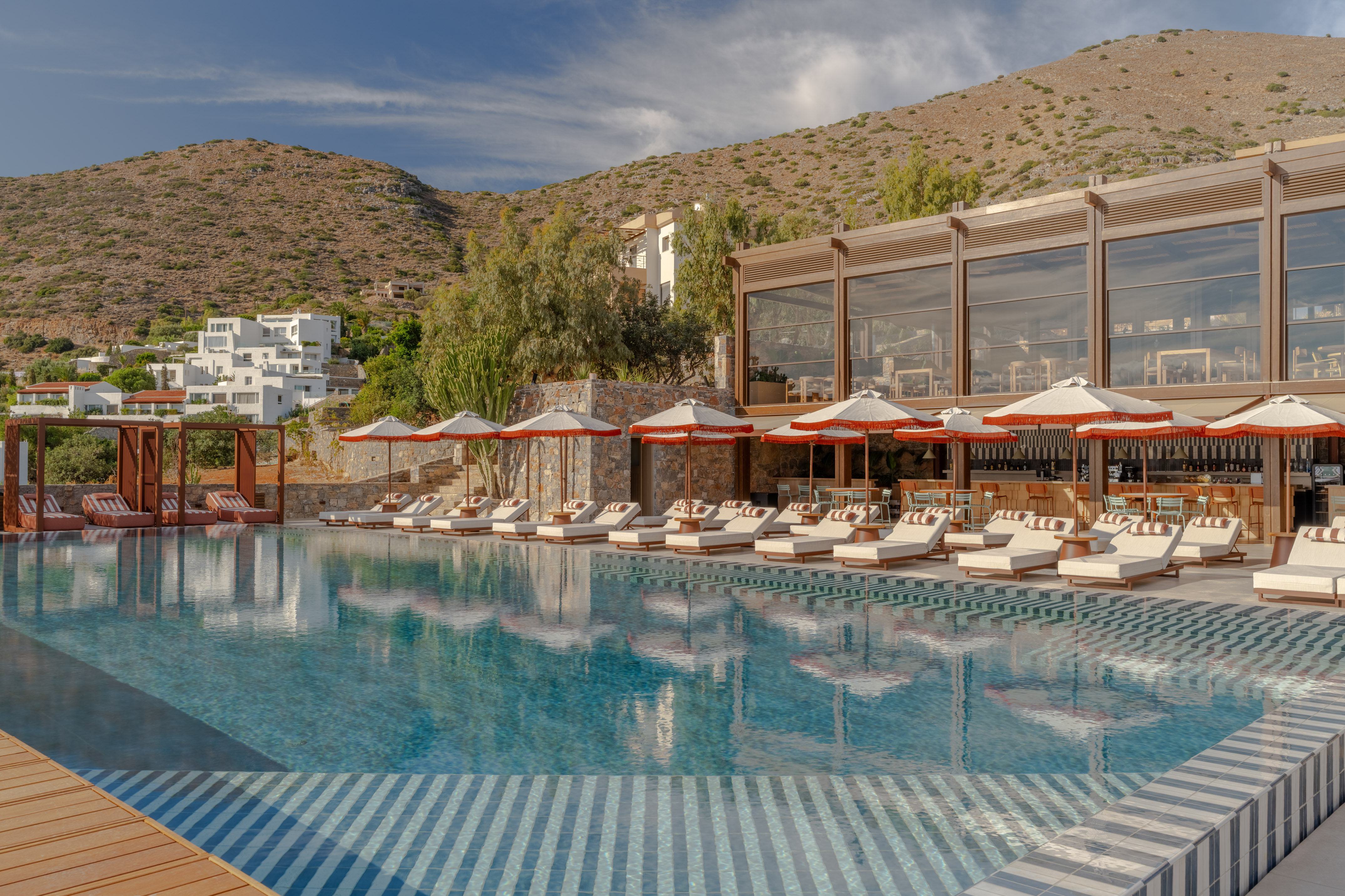Luxury resort pool with sun loungers, umbrellas, and mountain views.