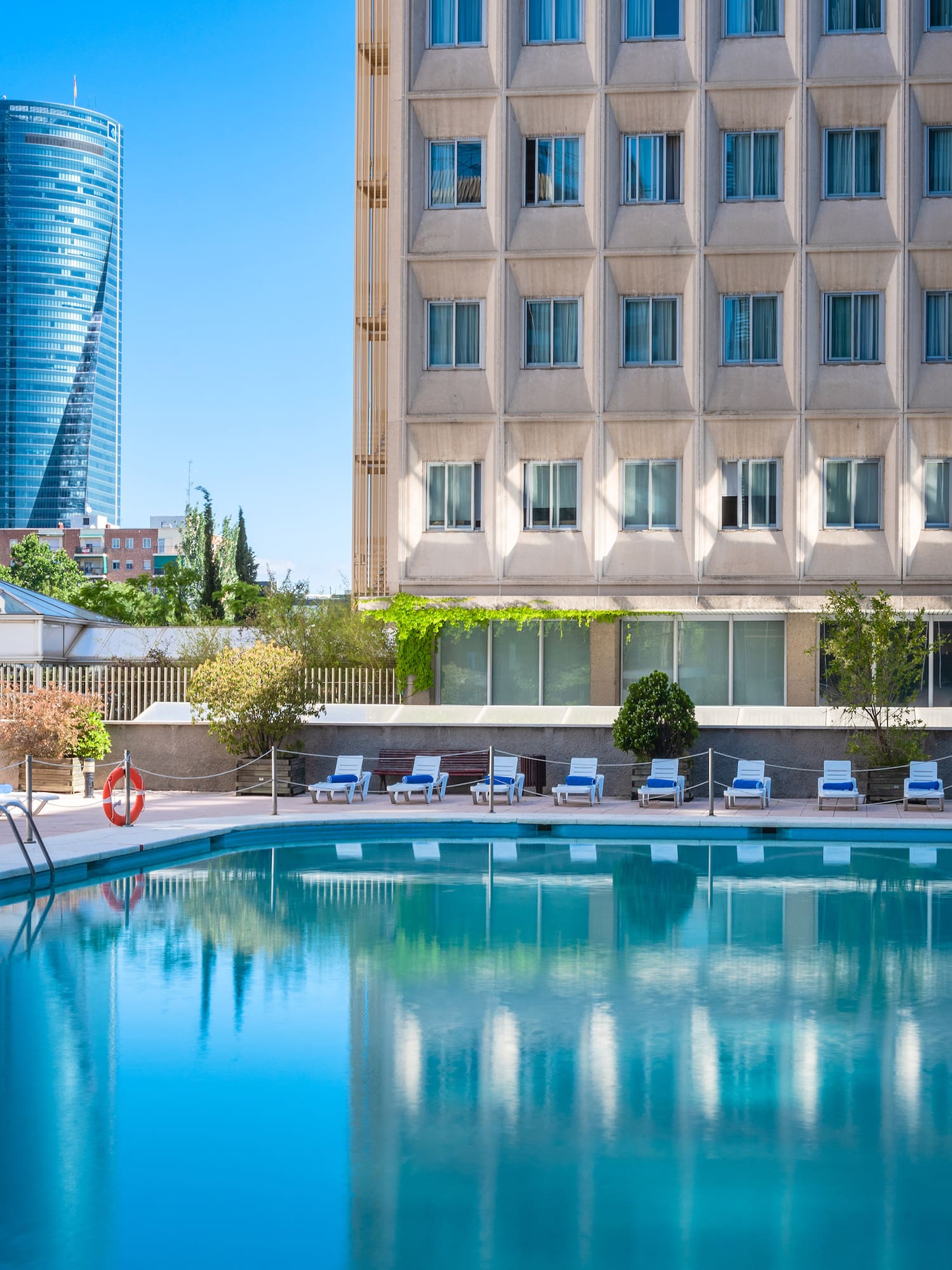 Resort swimming pool with sun loungers, modern hotel, and city skyscraper.