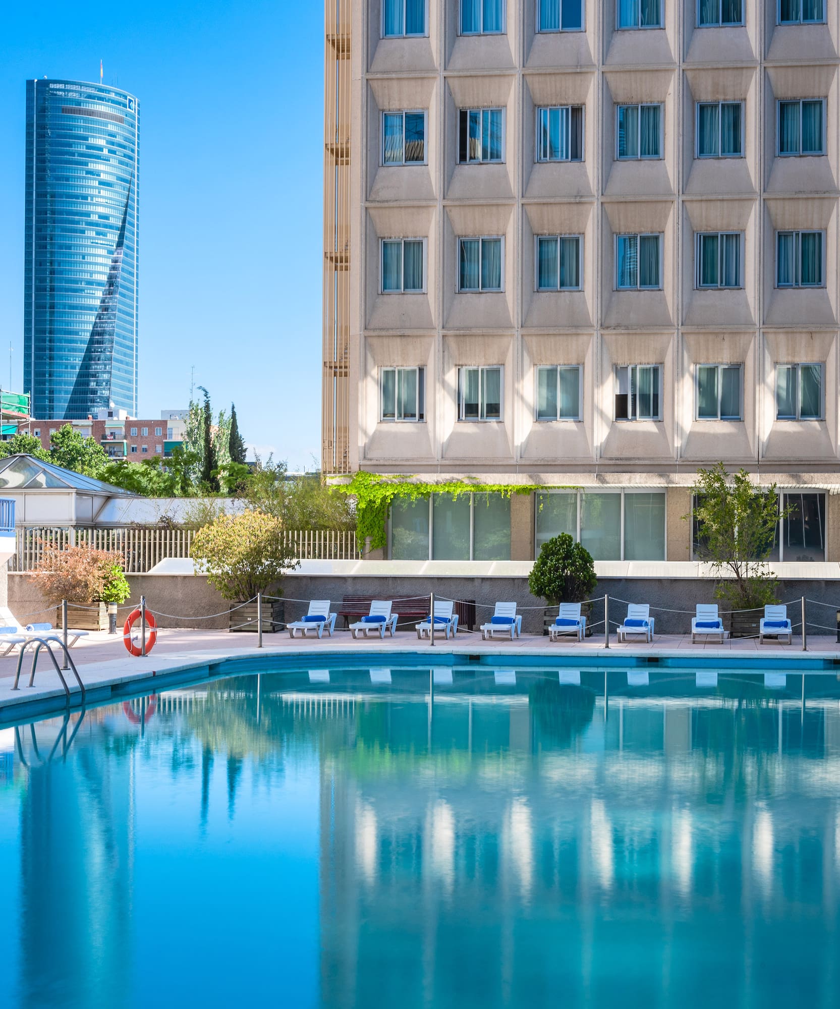 Resort swimming pool with sun loungers, modern hotel, and city skyscraper.