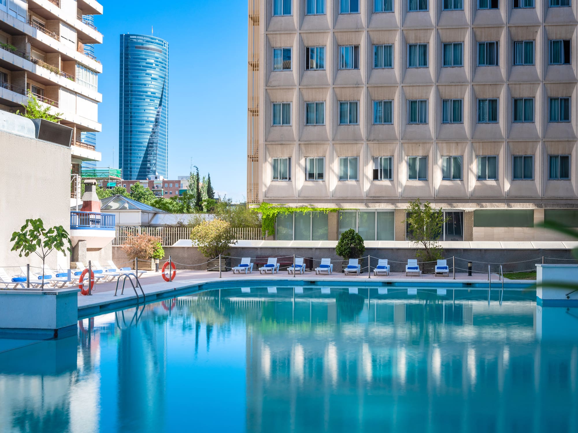 Urban hotel pool with clear blue water, sun loungers, and city buildings.