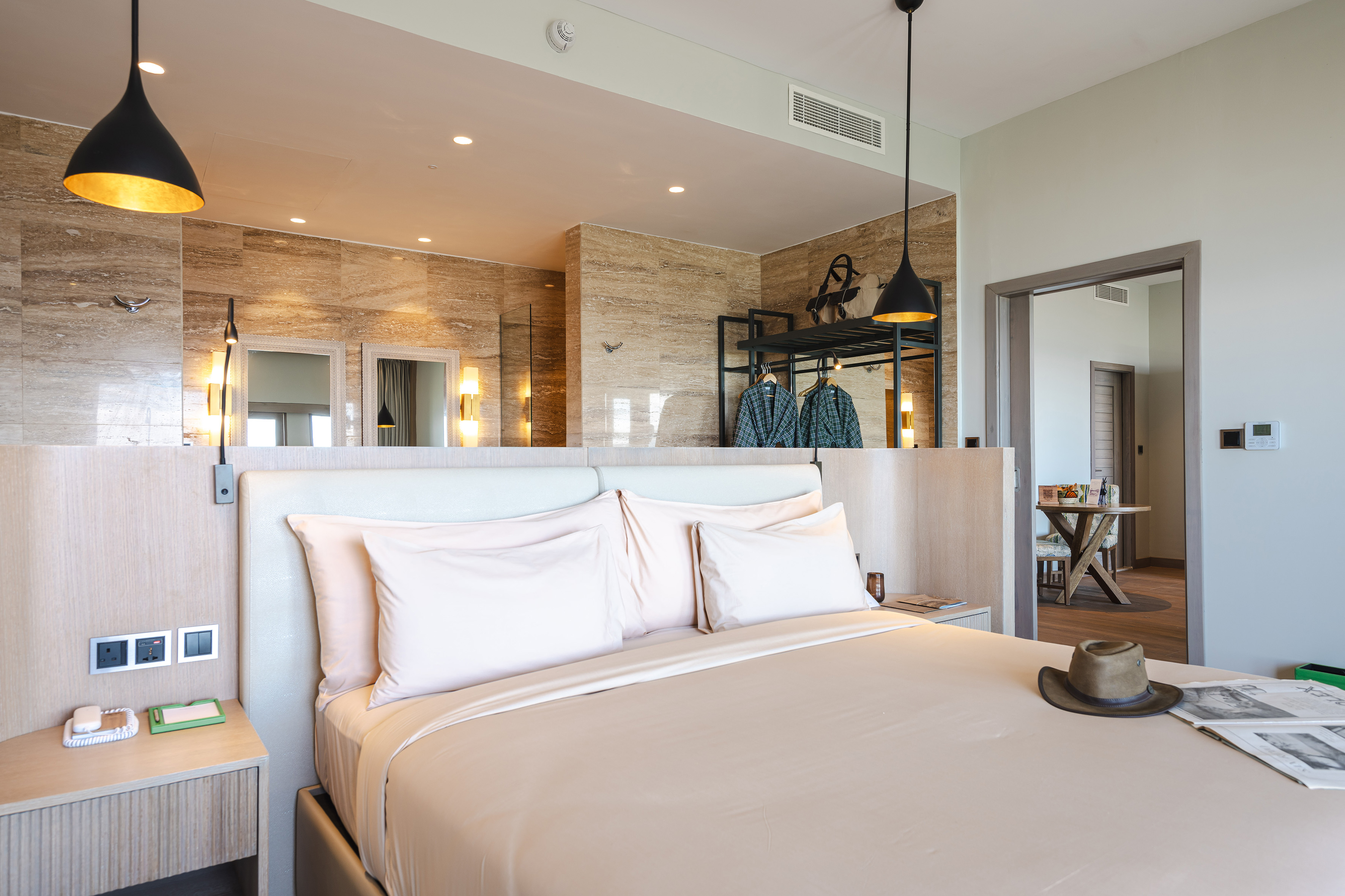 Modern hotel bedroom with neutral tones, elegant pendant lights, and open closet.