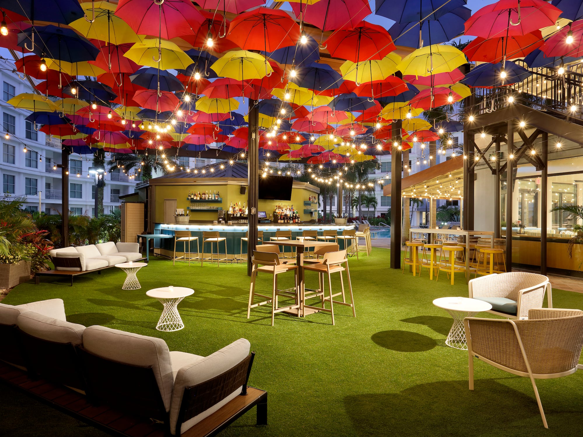 Colorful umbrella canopy over an outdoor bar and lounge with string lights.