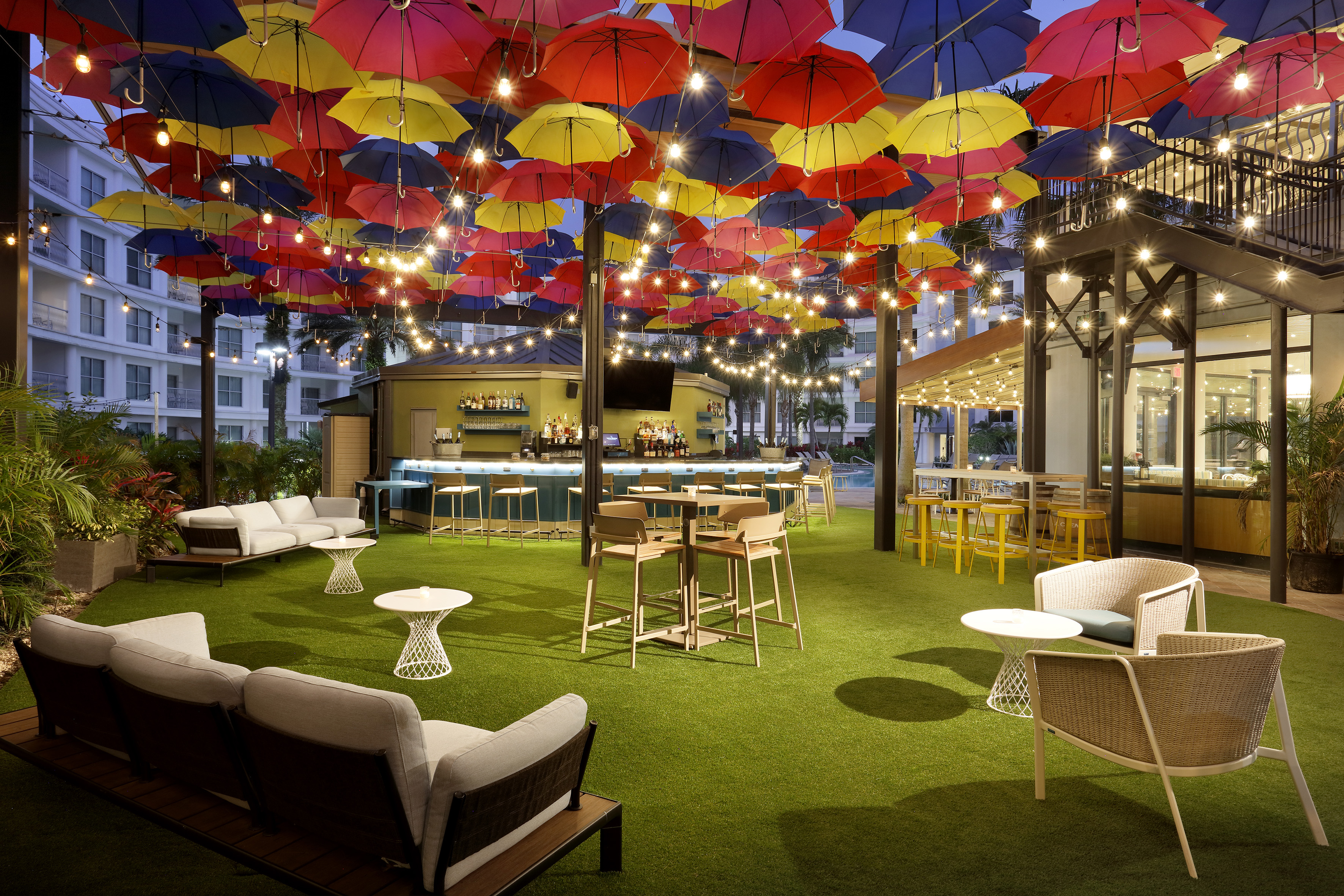 Colorful umbrella canopy over an outdoor bar and lounge with string lights.