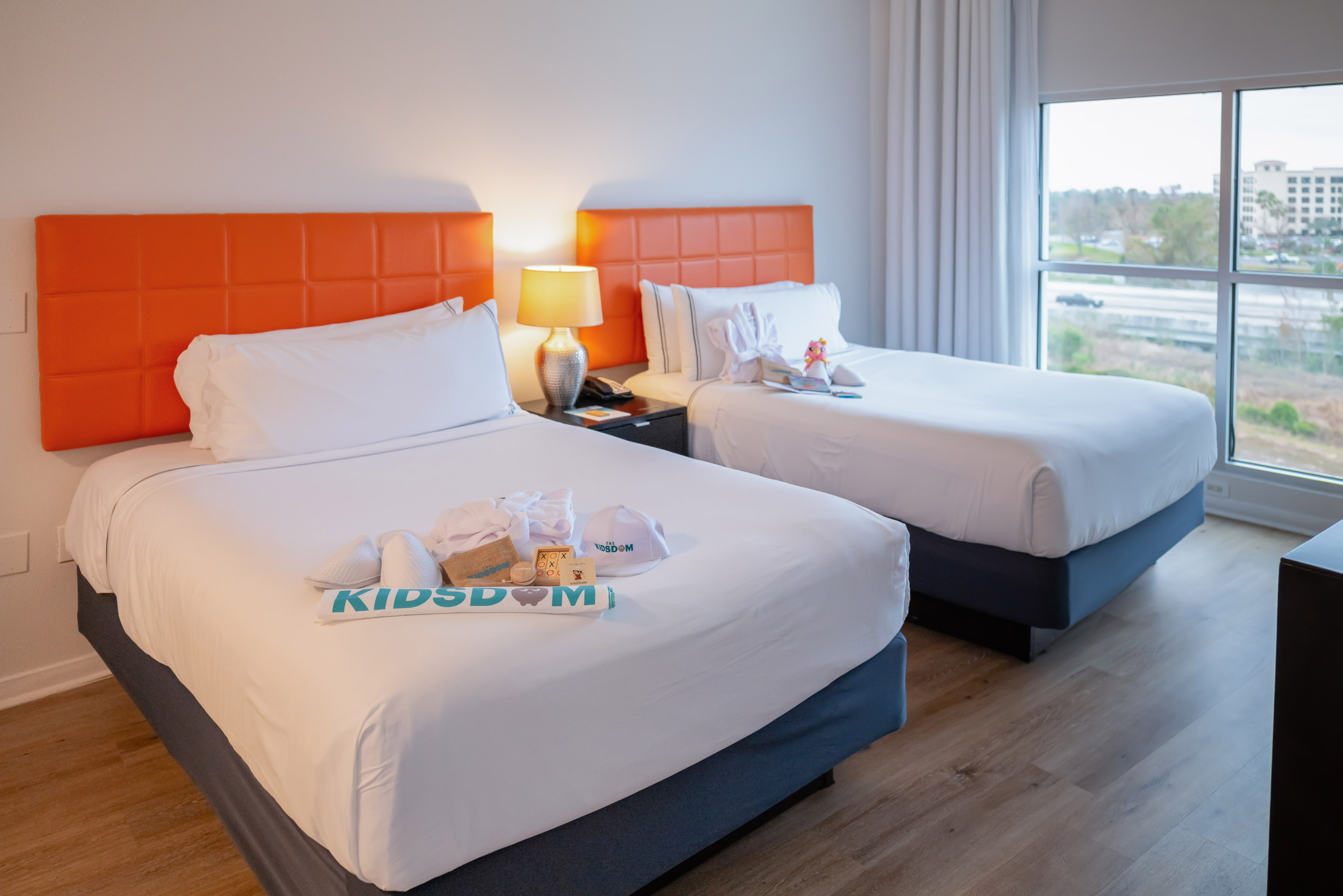 Kids hotel room with two beds, orange headboards, and Kidsdom welcome kit.