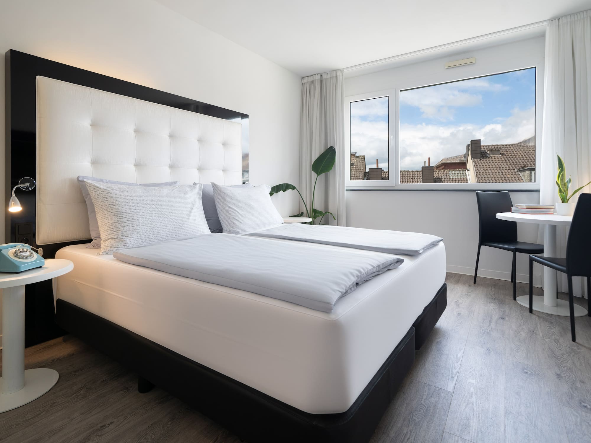 Bright modern hotel room with twin beds, white headboard, city view, and dining.