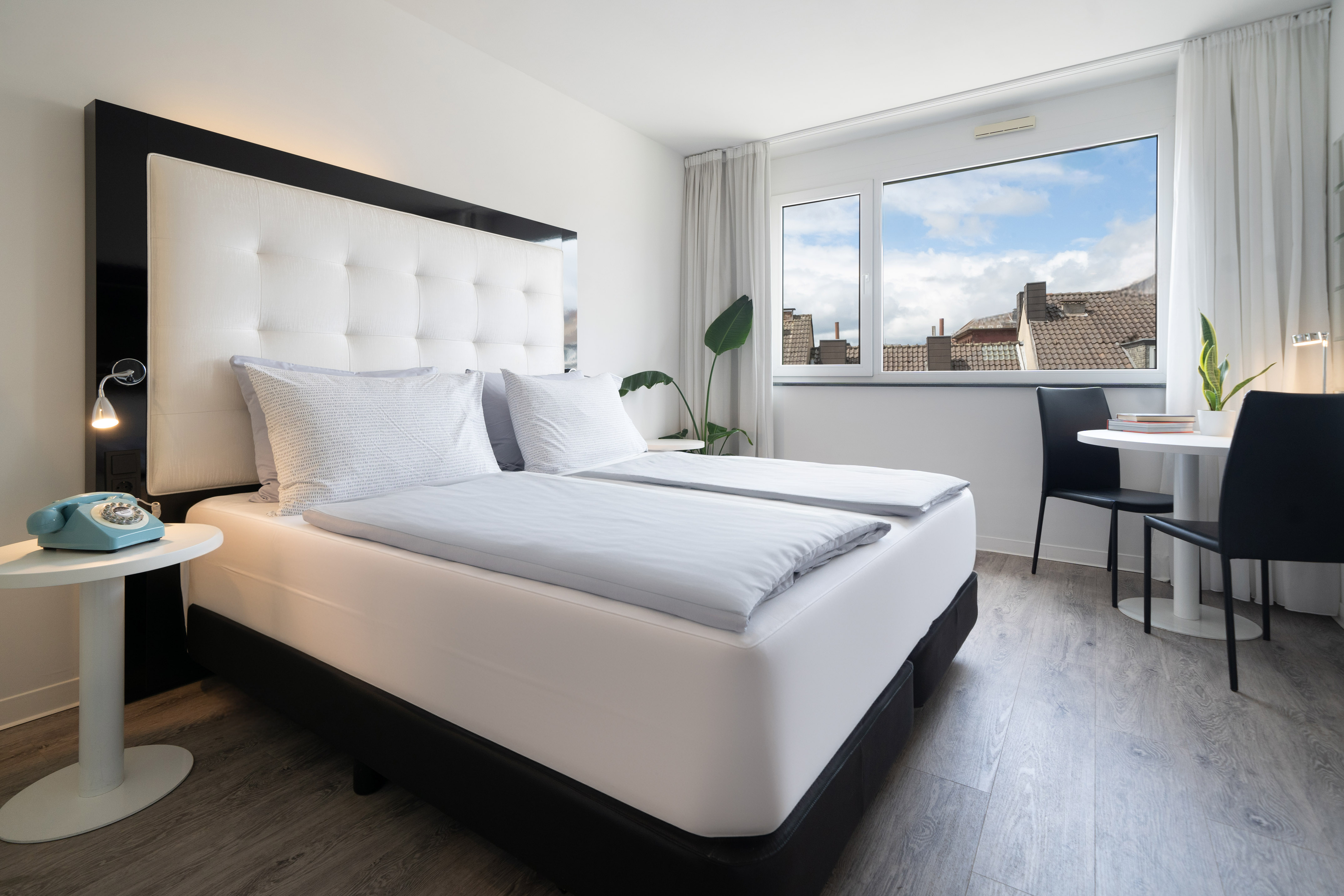Bright modern hotel room with twin beds, white headboard, city view, and dining.