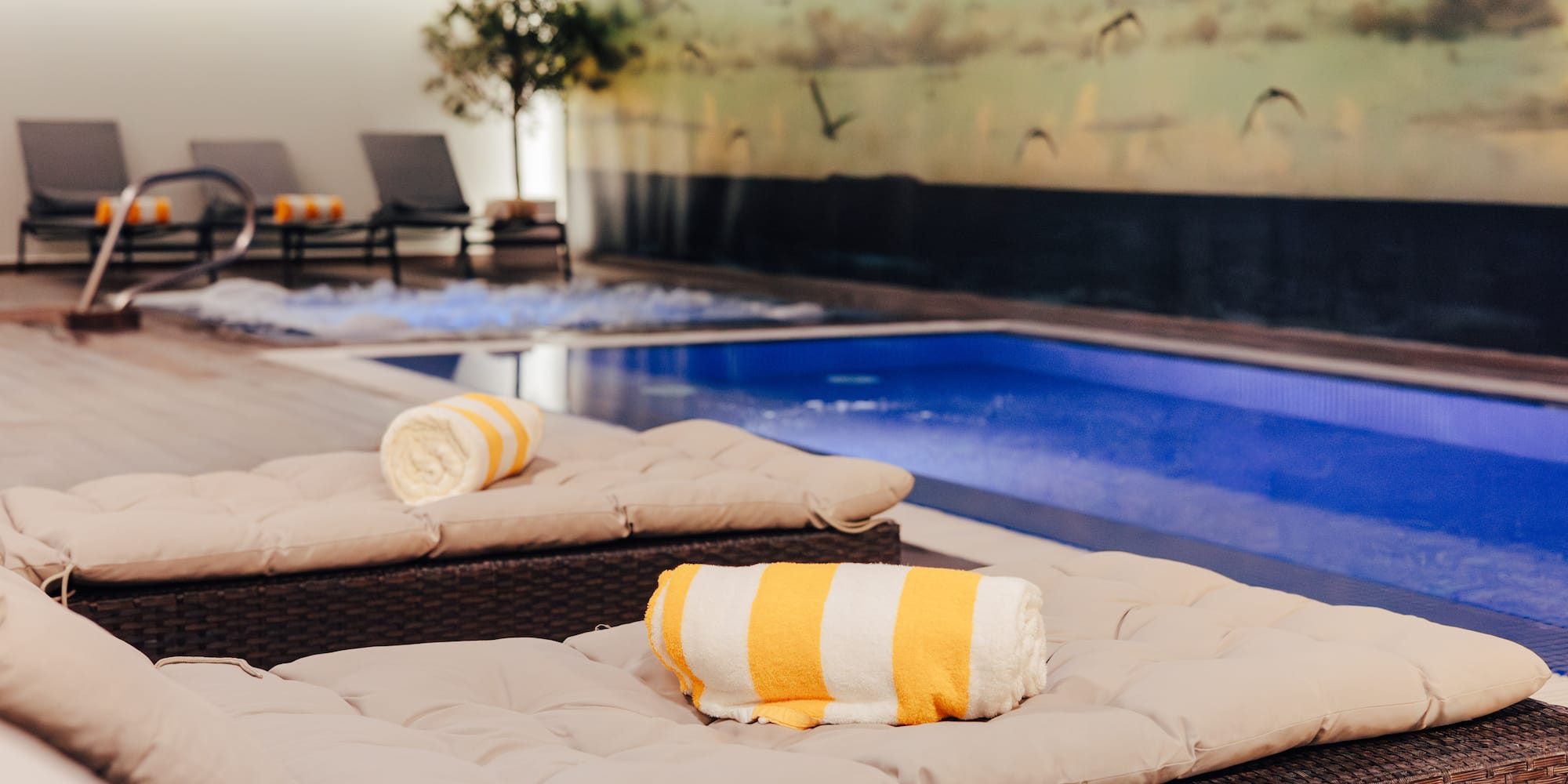 Indoor hotel pool area with lounge chairs, yellow towels, and a jacuzzi.