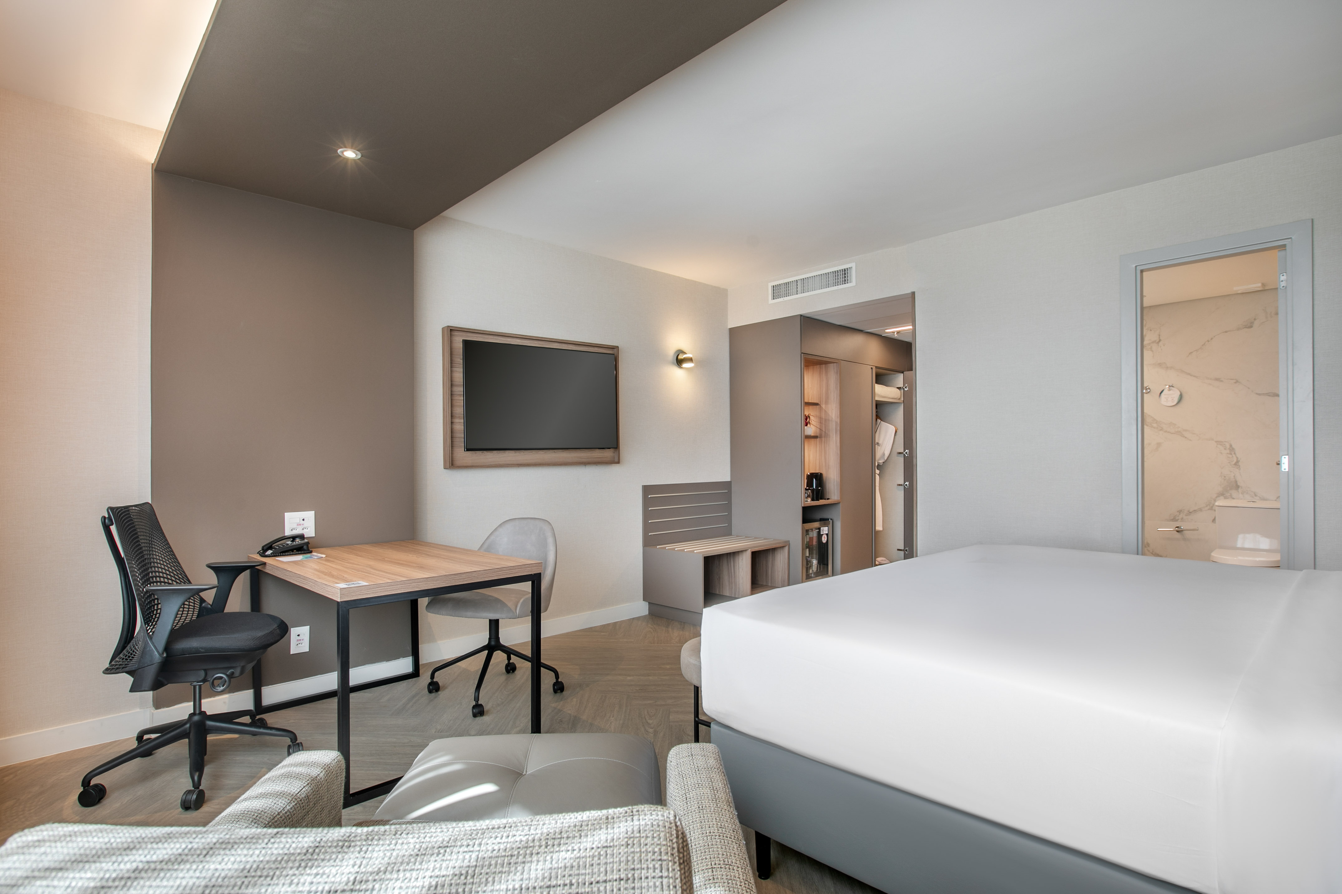 Contemporary hotel room with king bed, work desk, wall TV, and open closet.