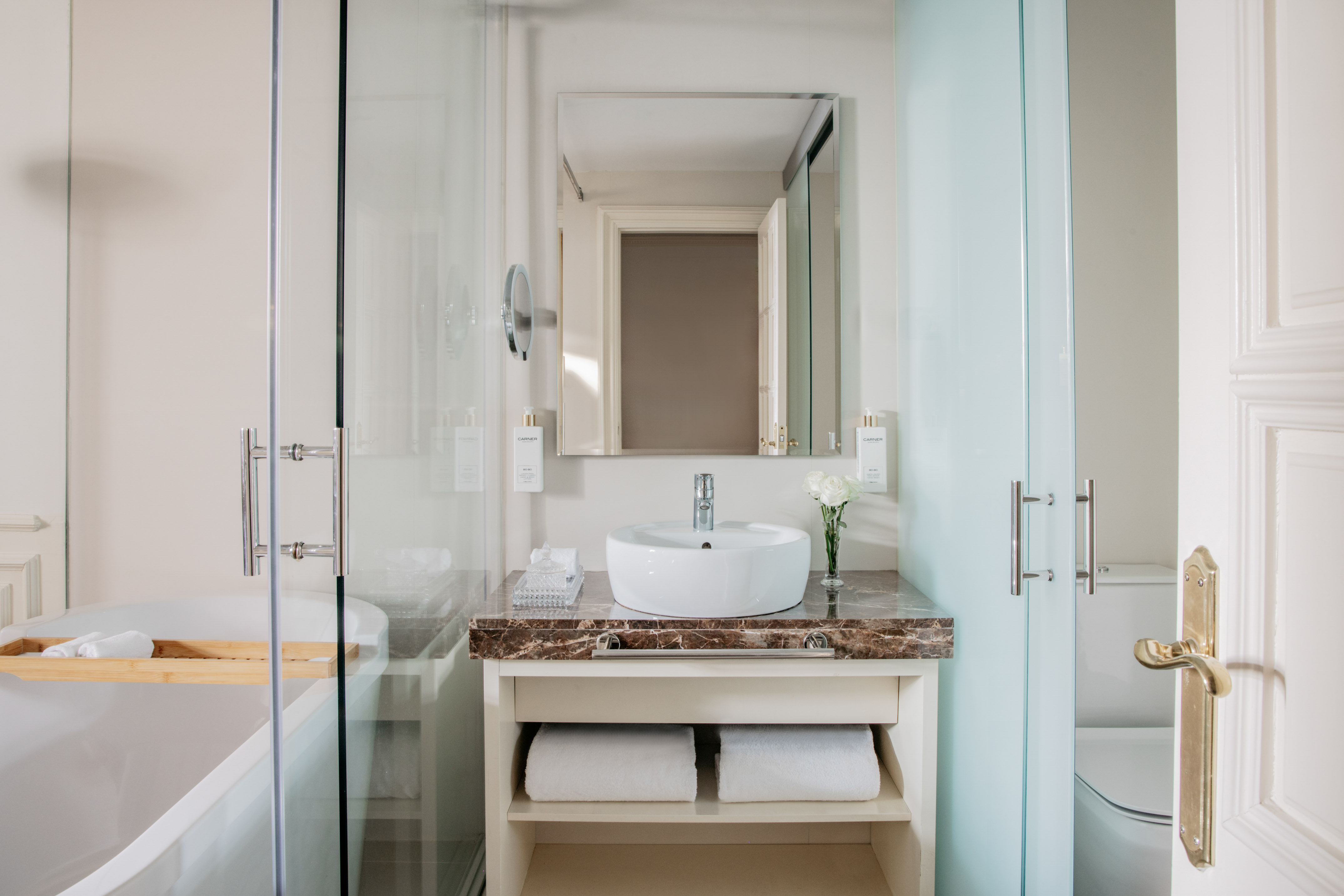Modern bathroom with vanity sink, marble counter, large mirror, and glass enclosed bathtub.