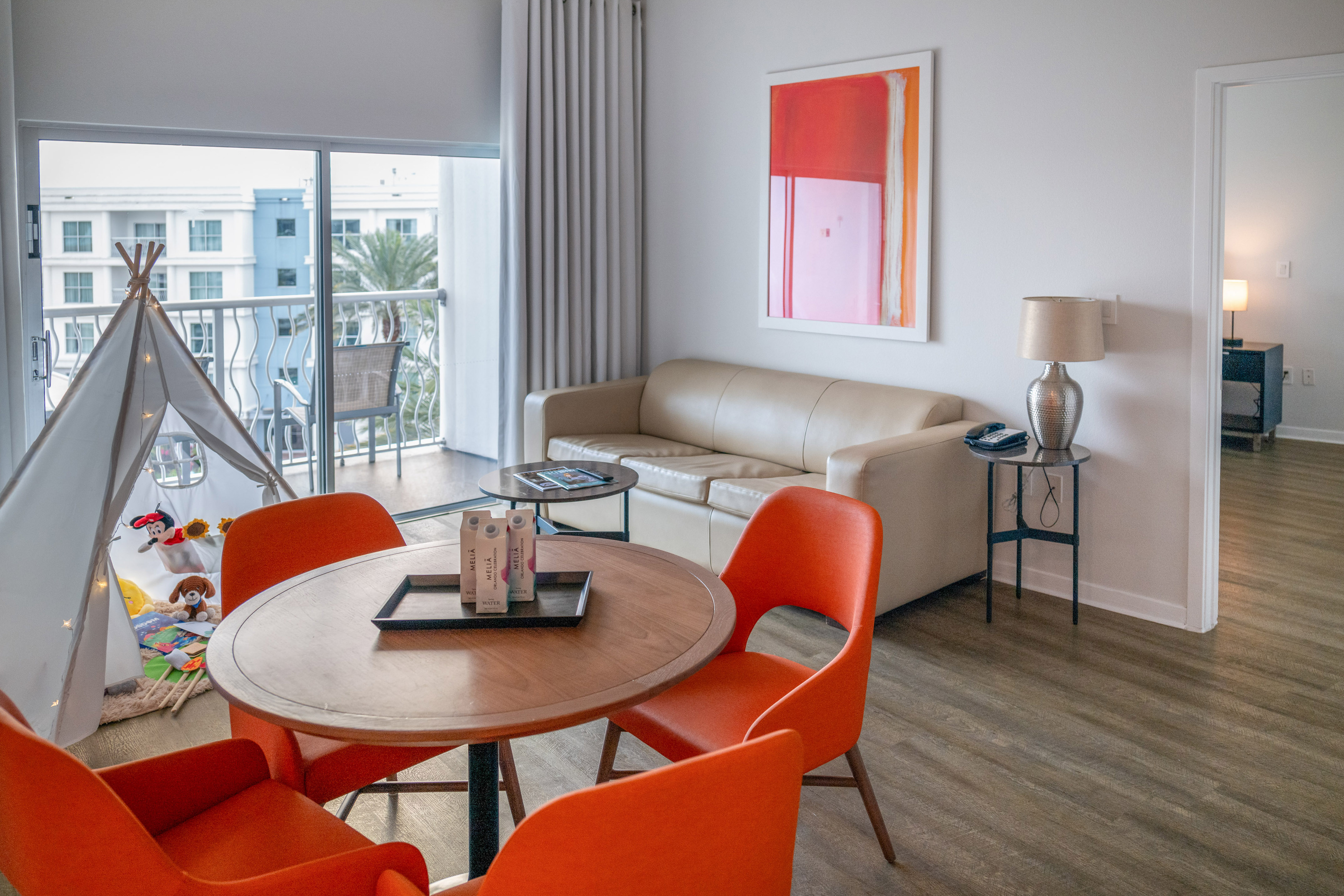Modern hotel living room with sofa, orange dining, kids' teepee, and balcony. - The Level Family Suite - Meliá Orlando Celebration, Orlando