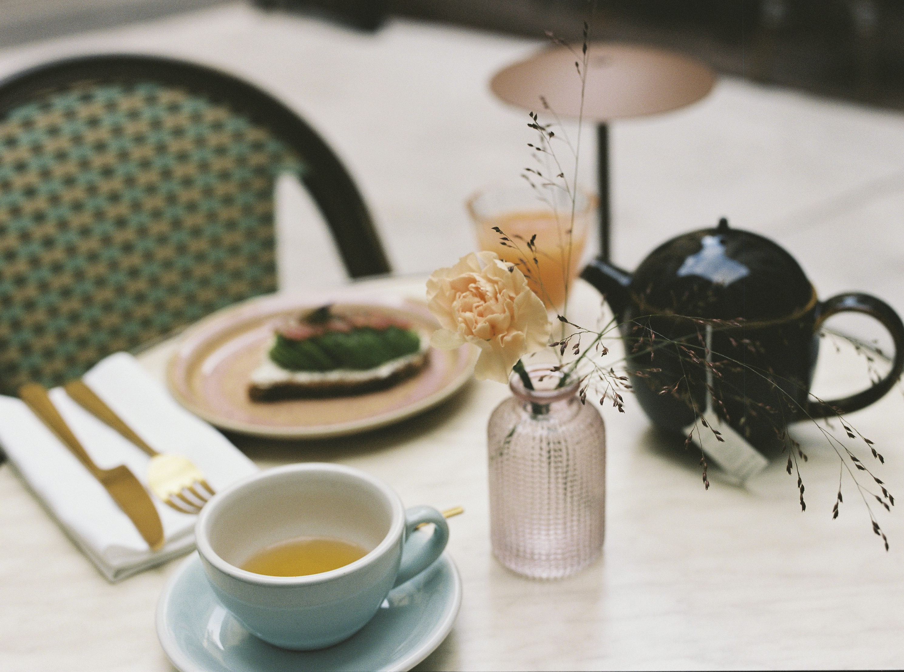Elegant breakfast table with tea, avocado toast, juice, and a flower.