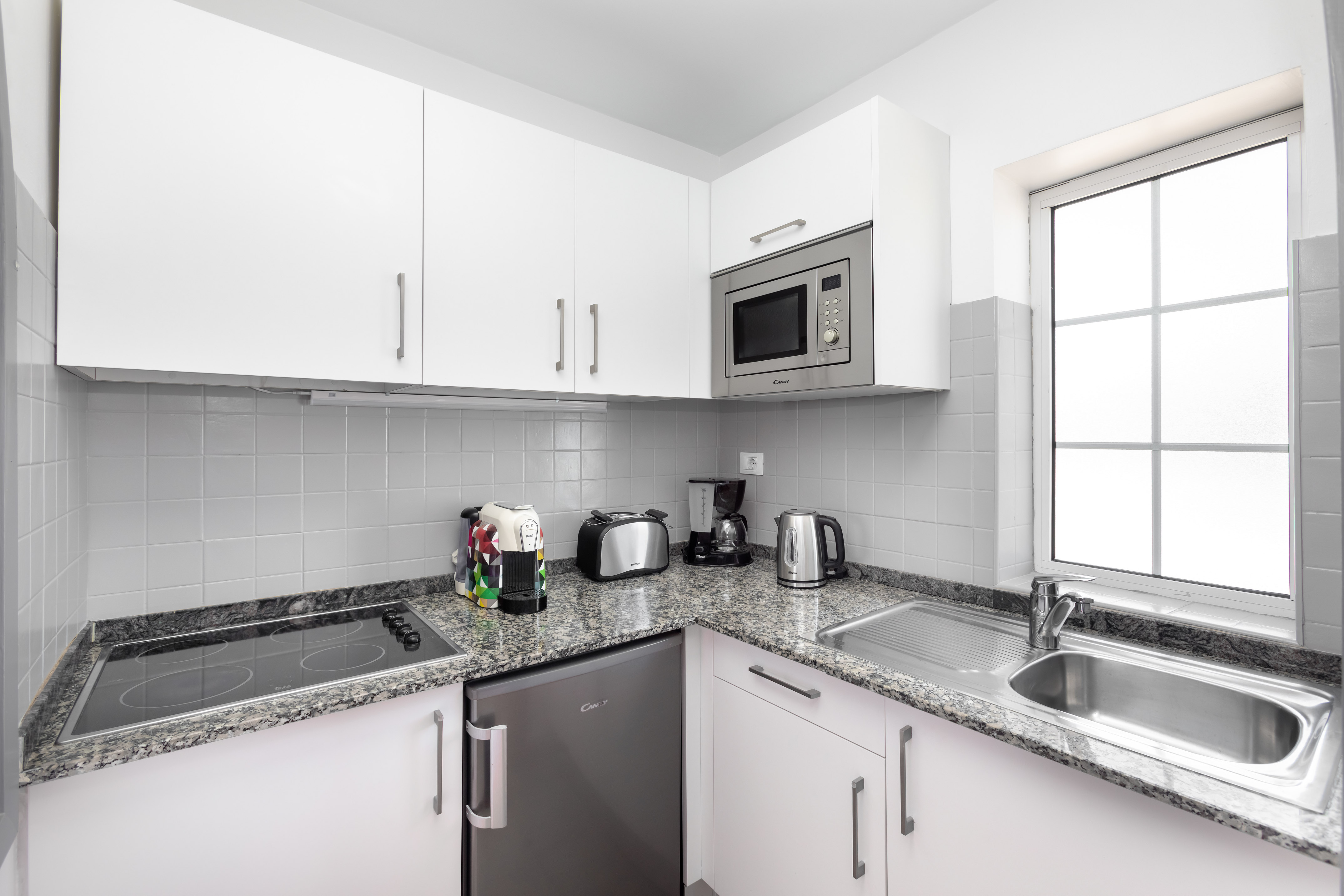 Modern compact kitchen with white cabinets, granite counters, microwave, and appliances.