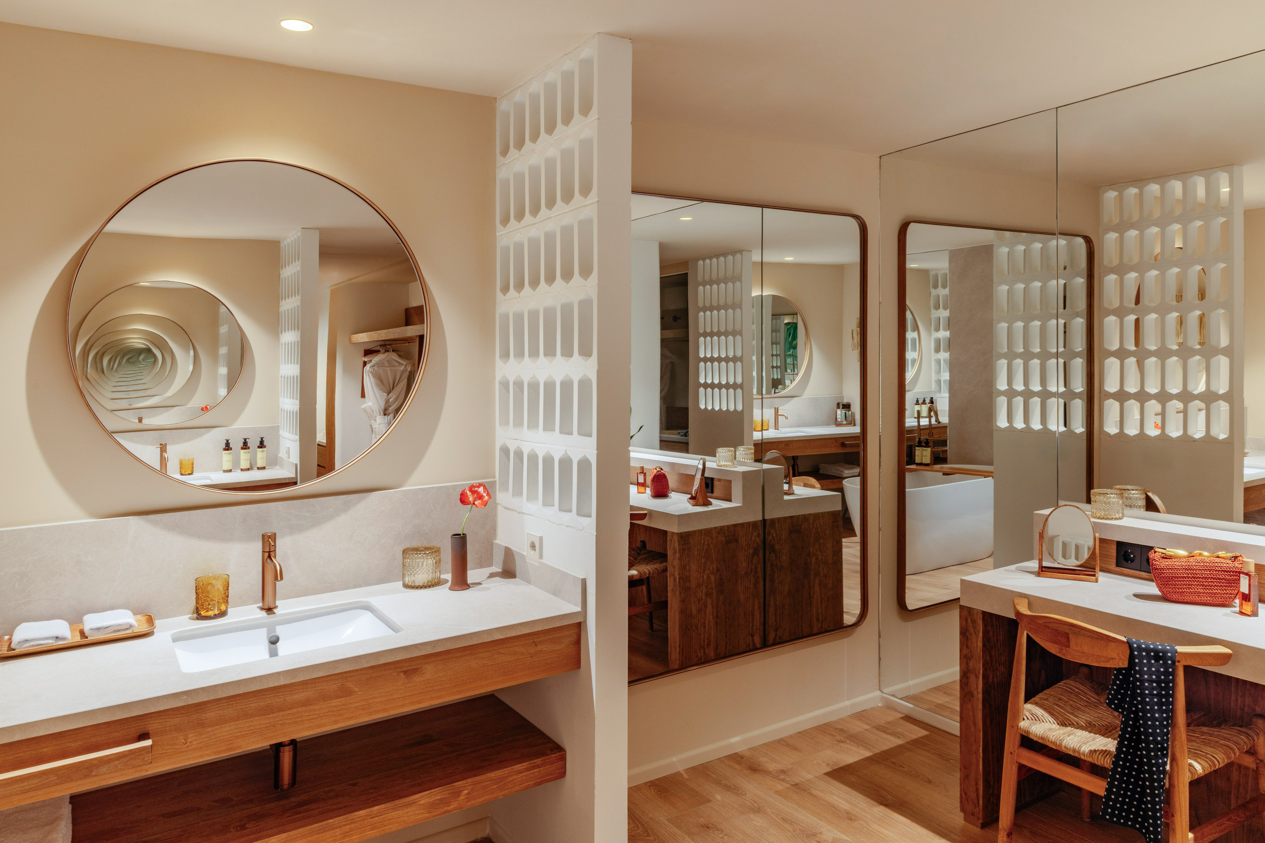 Modern hotel bathroom with wood vanity, circular mirror, and decorative screen.