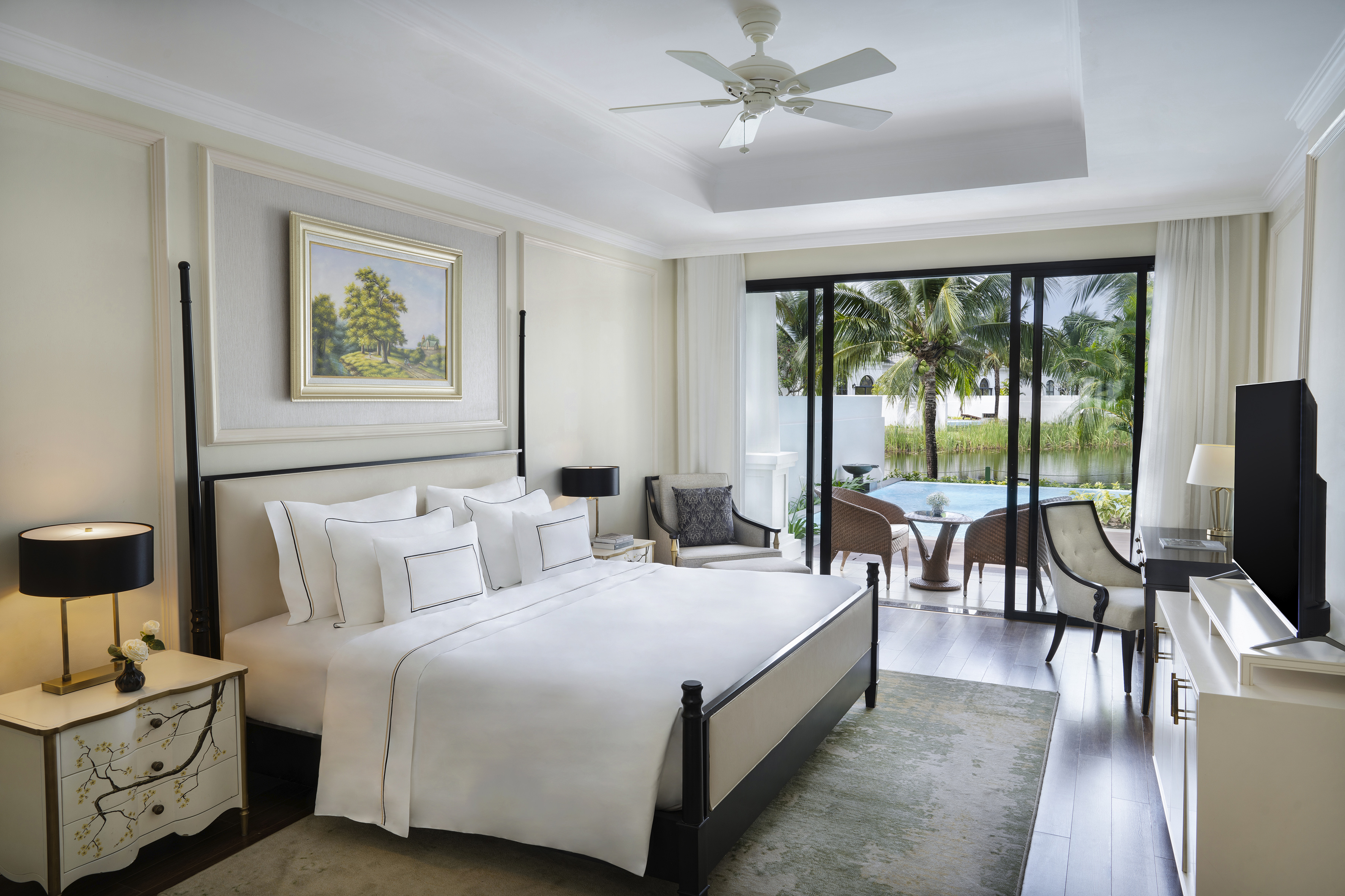 Luxury hotel bedroom with king bed, private patio, and tropical pool view.