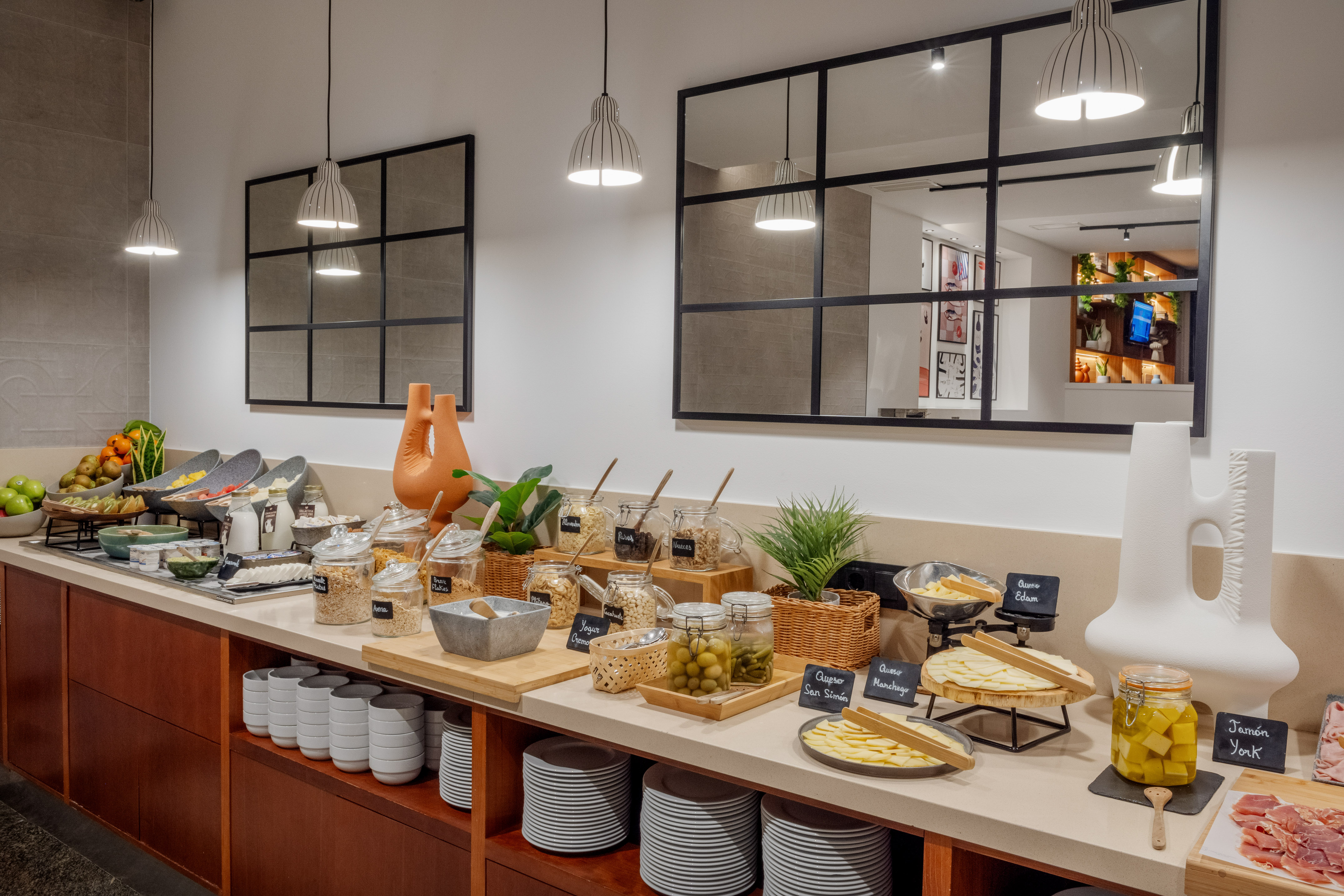 Hotel breakfast buffet offering diverse fresh fruit, cereals, cheese, ham, and olives.