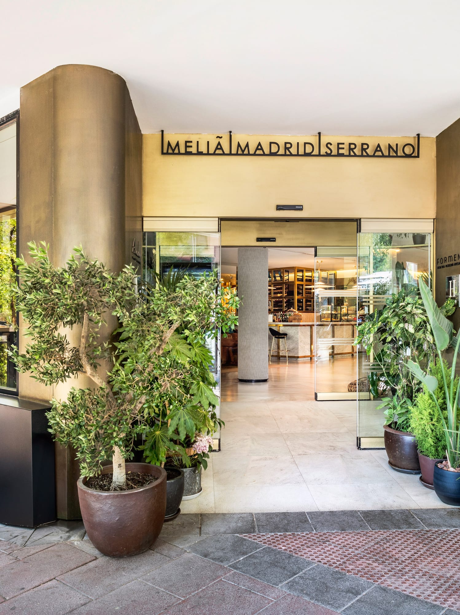 Meliã Madrid Serrano hotel entrance with glass doors, modern facade, and potted plants.