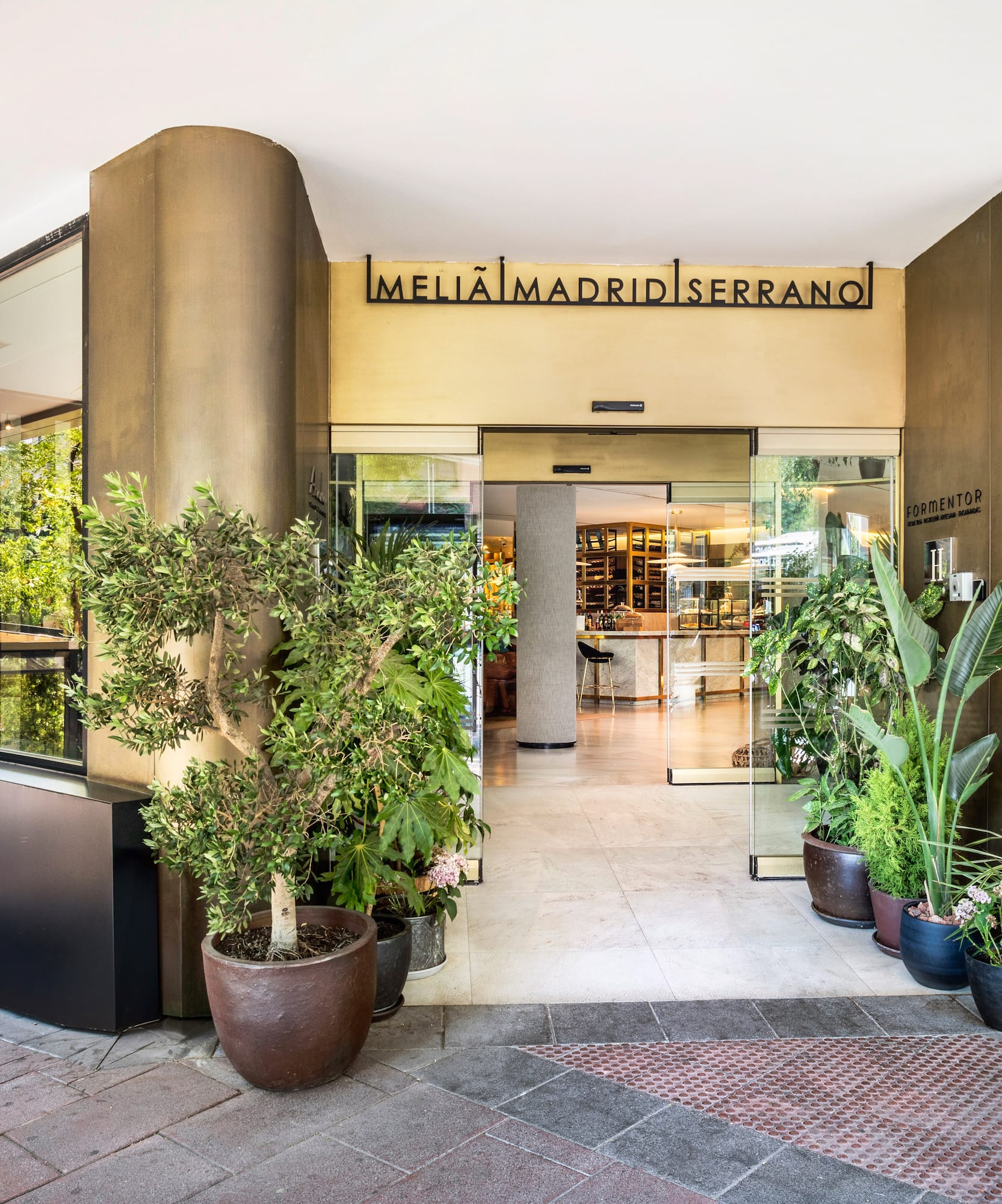 Meliã Madrid Serrano hotel entrance with glass doors, modern facade, and potted plants.